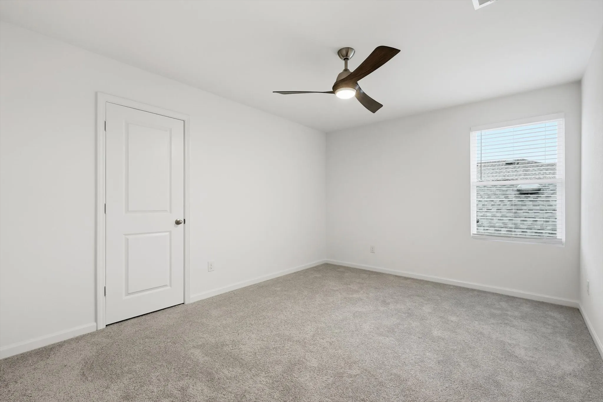 Neutral-toned carpeted room featuring a ceiling fan with integrated lighting, a single window with blinds, and white walls