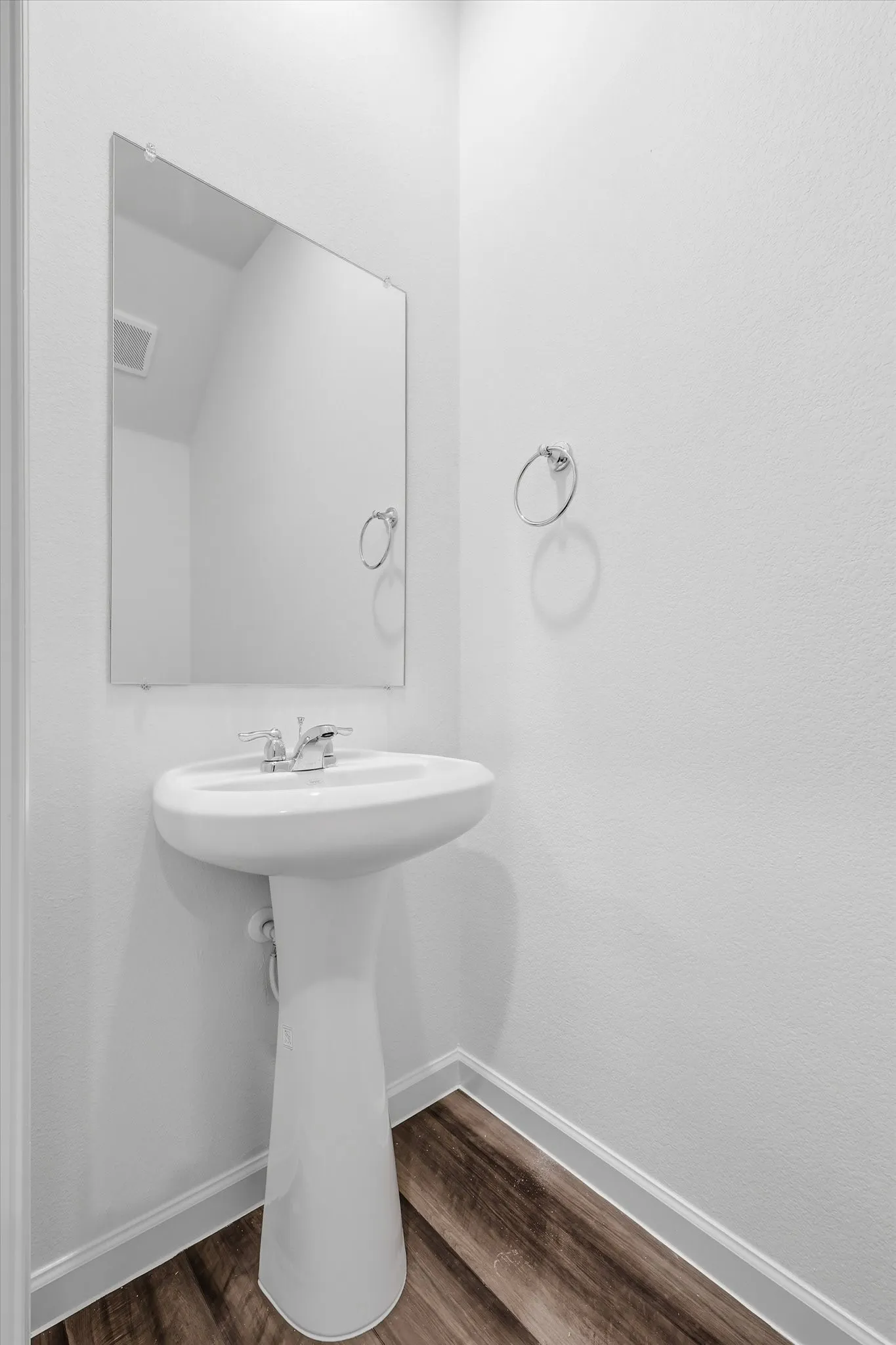 Pedestal sink with a chrome faucet, frameless mirror, and wood-finish flooring