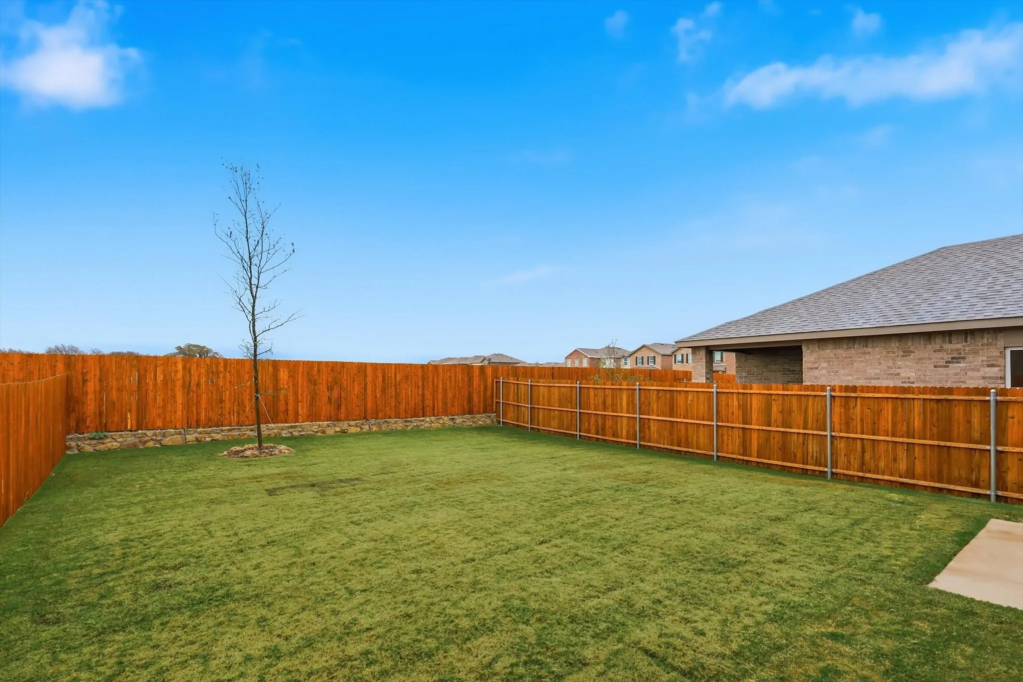 Expansive backyard featuring a lush lawn, privacy fencing, and a mature tree