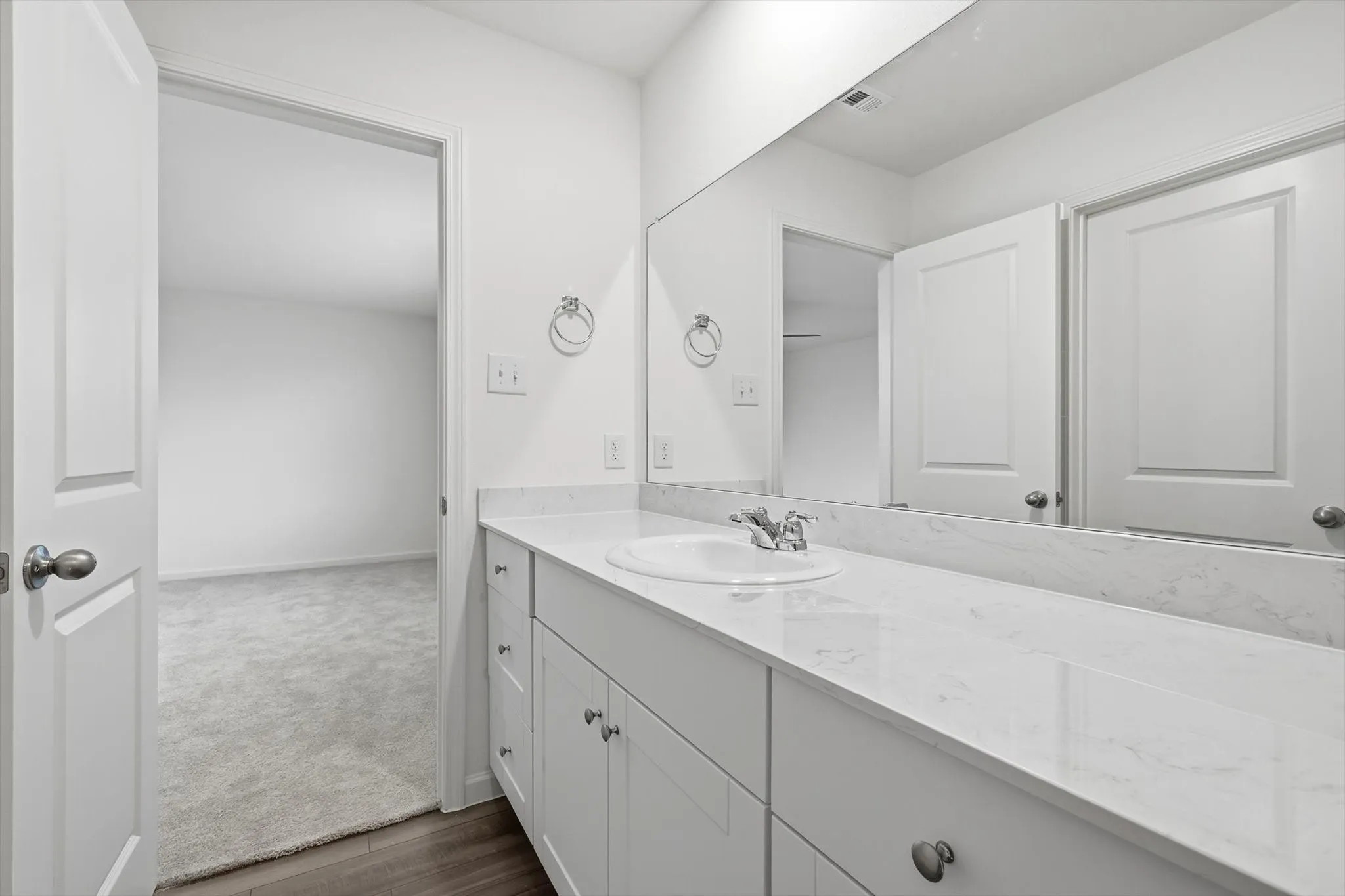 Bathroom vanity featuring white cabinetry, a single undermount sink, a polished chrome faucet, and a full-width wall mirror
