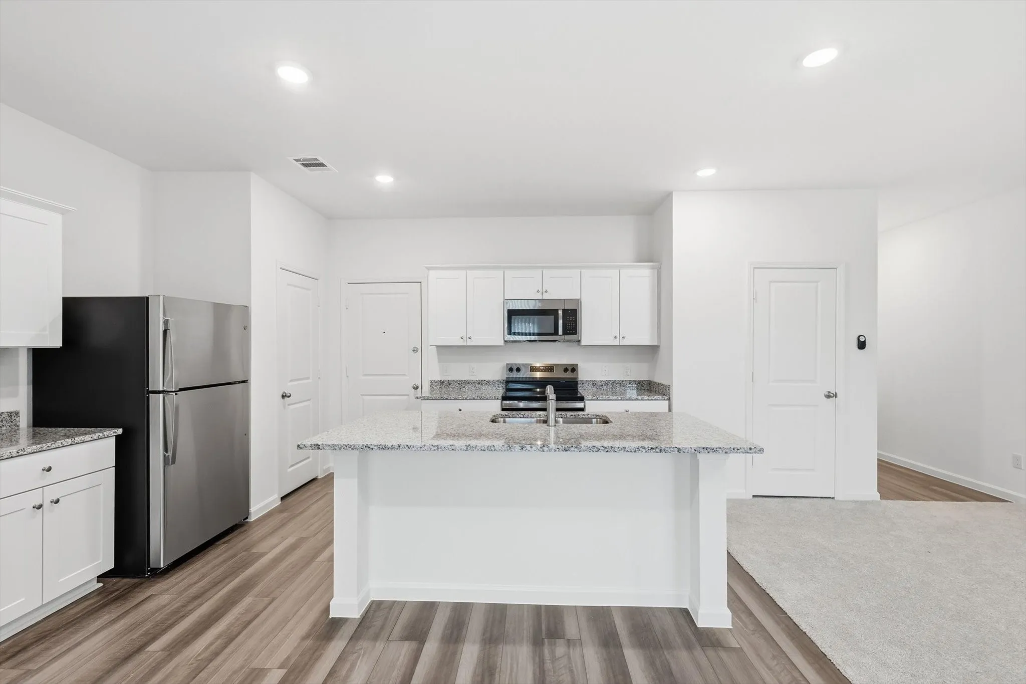 Kitchen featuring white cabinetry, stainless steel appliances, speckled countertops, a central island with an integrated sink, and recessed lighting