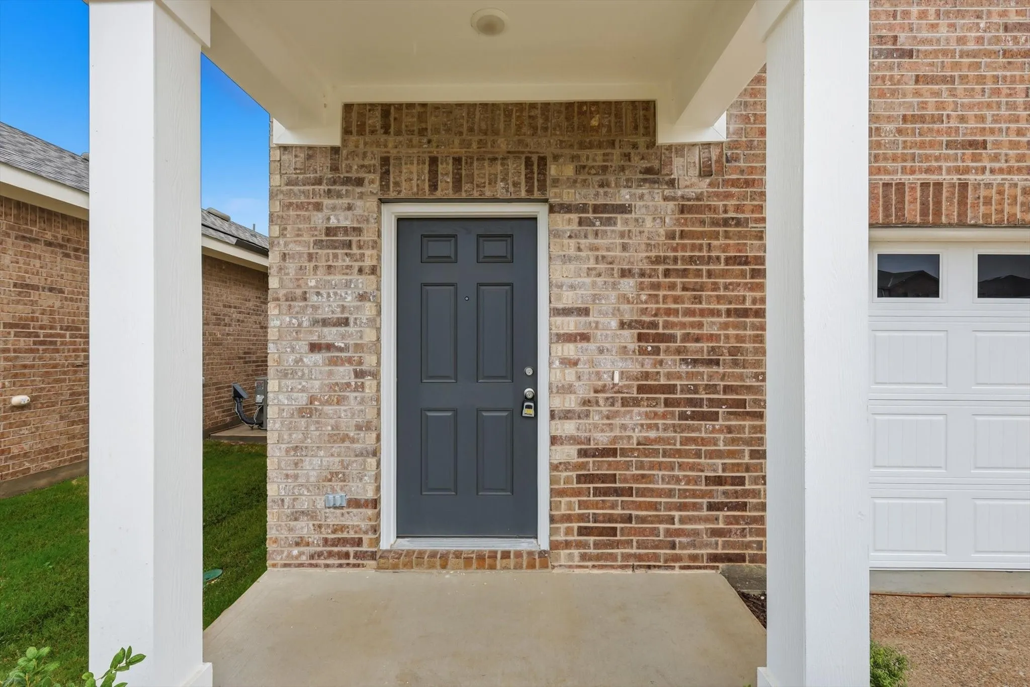Welcoming front entry featuring a paneled door, brick facade, and covered porch with white columns
