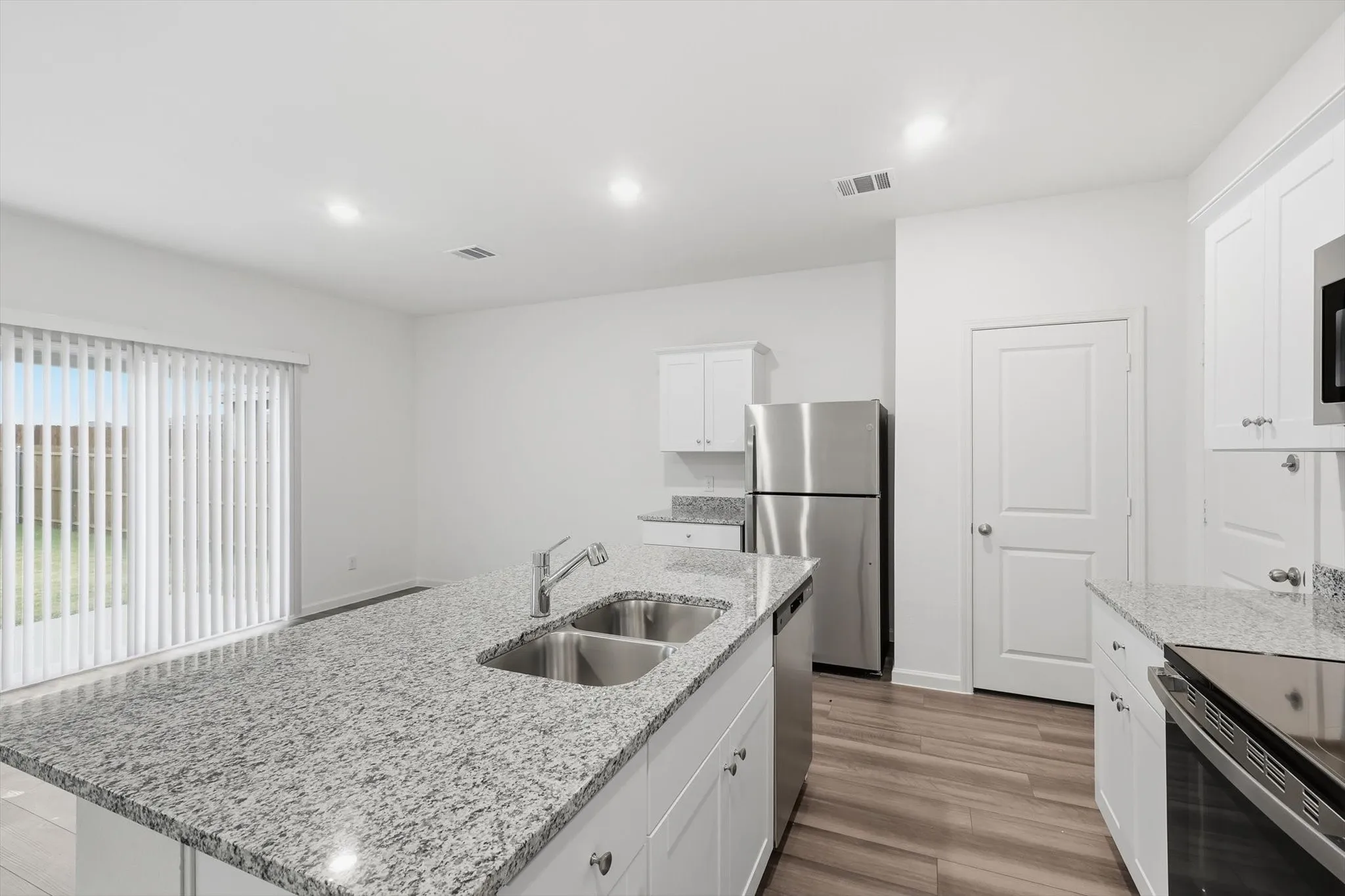 Kitchen featuring a central island with double stainless steel sinks, granite countertops, white cabinetry, stainless steel appliances, and wood-finish flooring