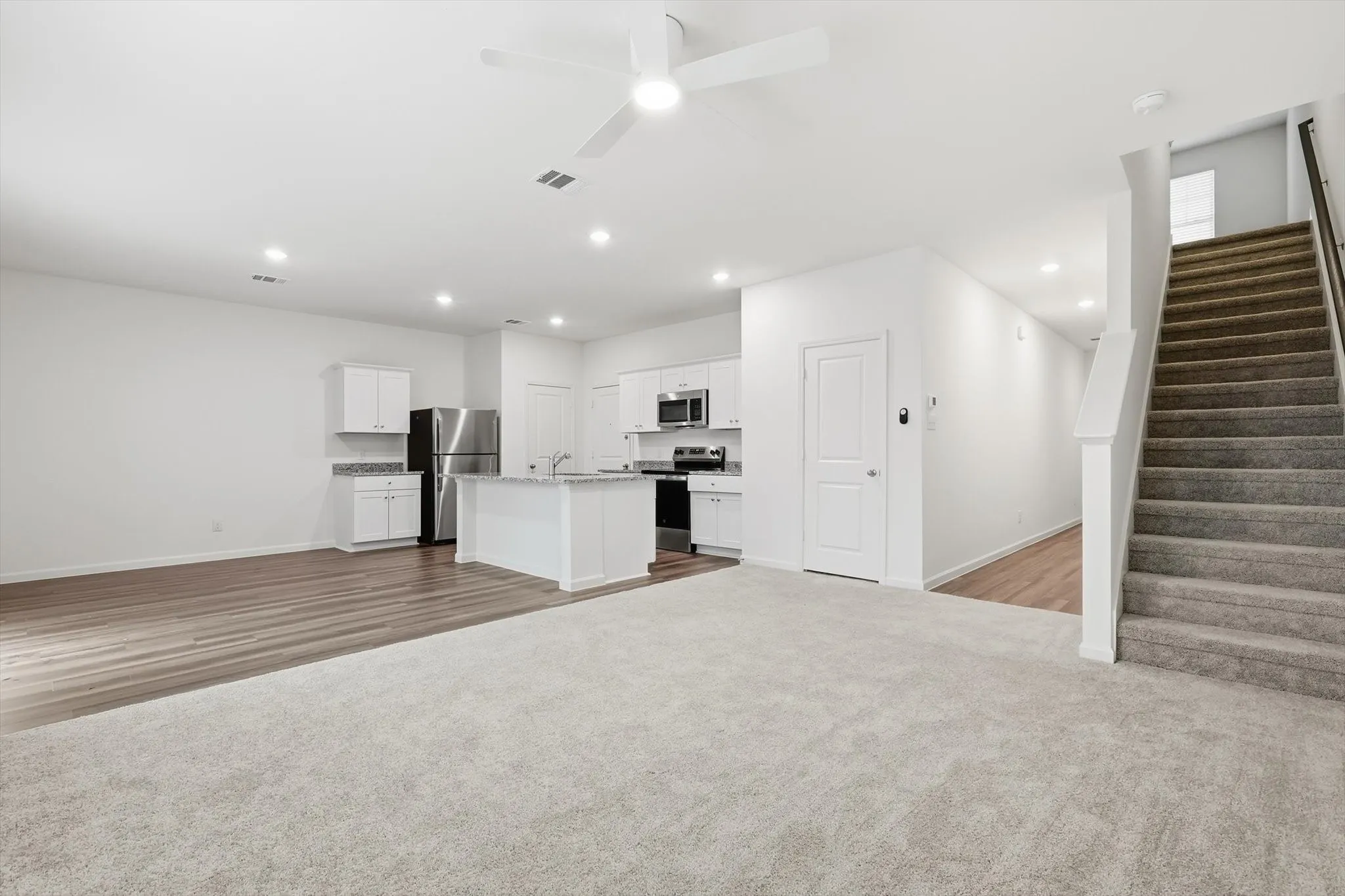 Open-concept living space featuring light-toned carpeting and wood-finish flooring