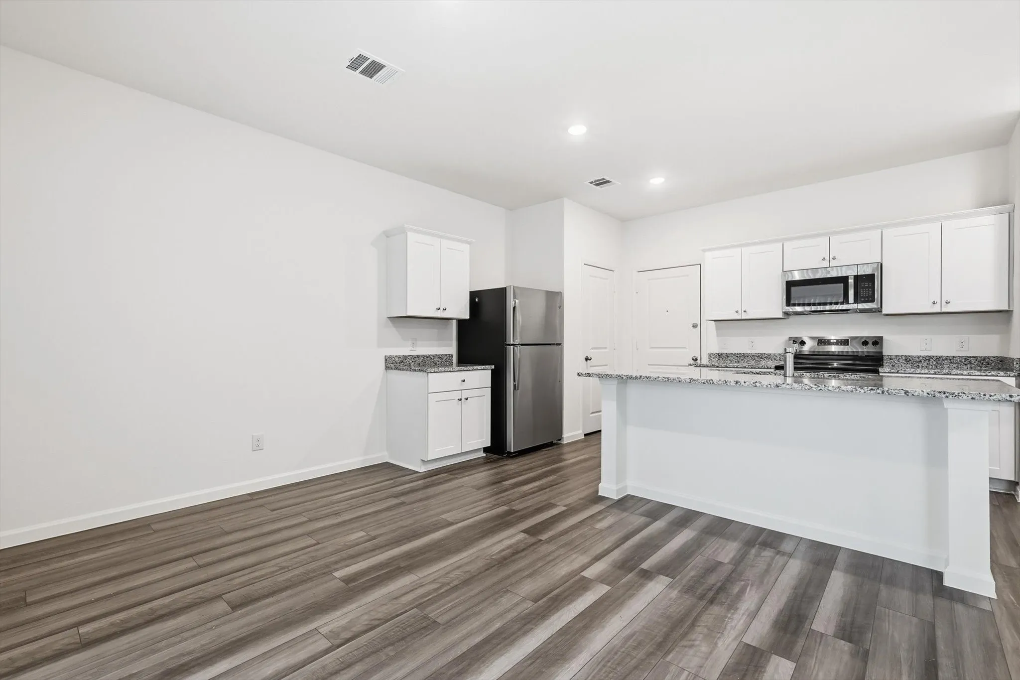 Open-concept kitchen featuring white cabinetry, granite countertops, stainless steel appliances, a kitchen island, and wood-finish flooring