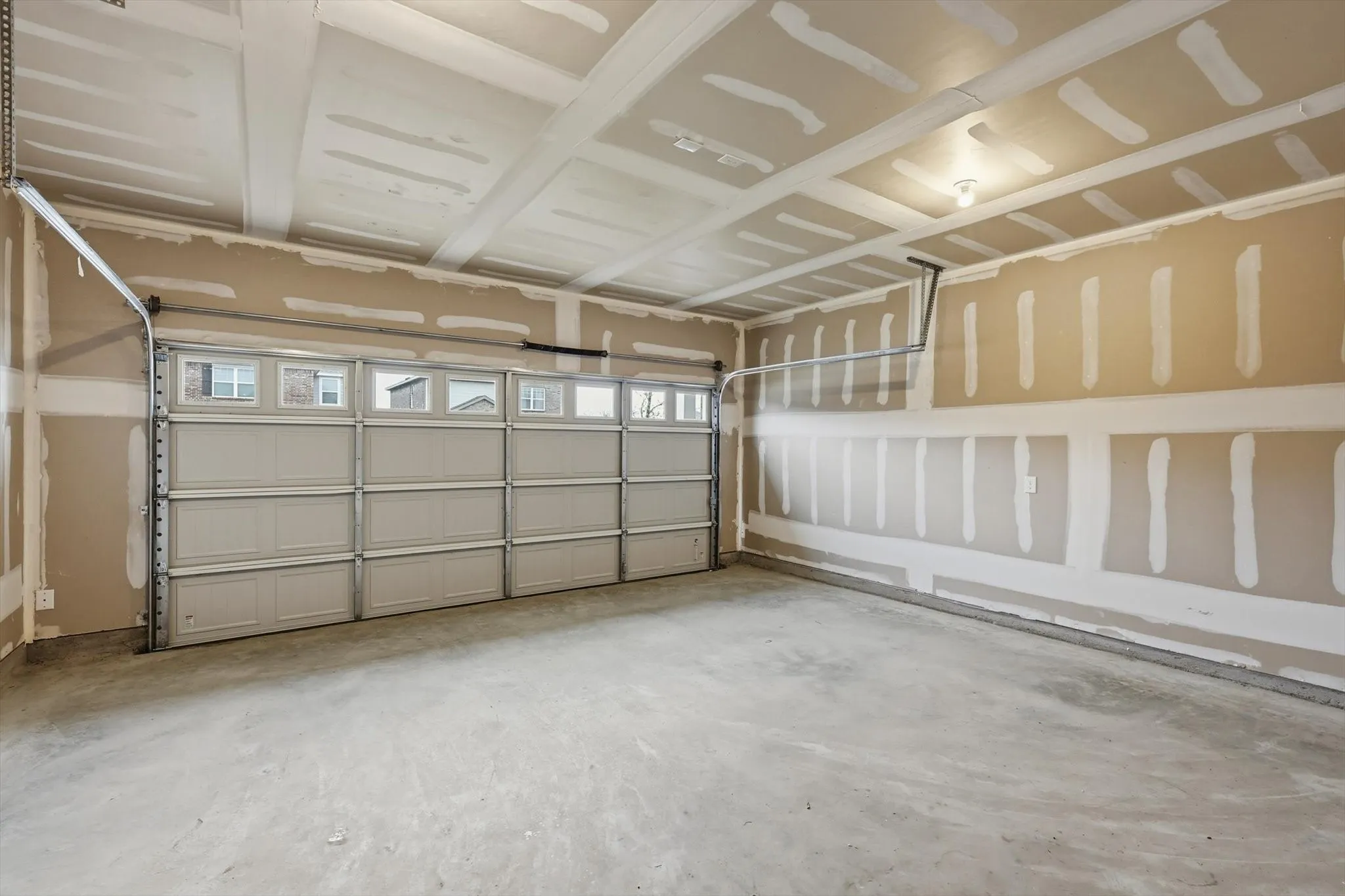 Two-car garage featuring a sectional garage door with upper window inserts, concrete flooring, and an exposed drywall finish