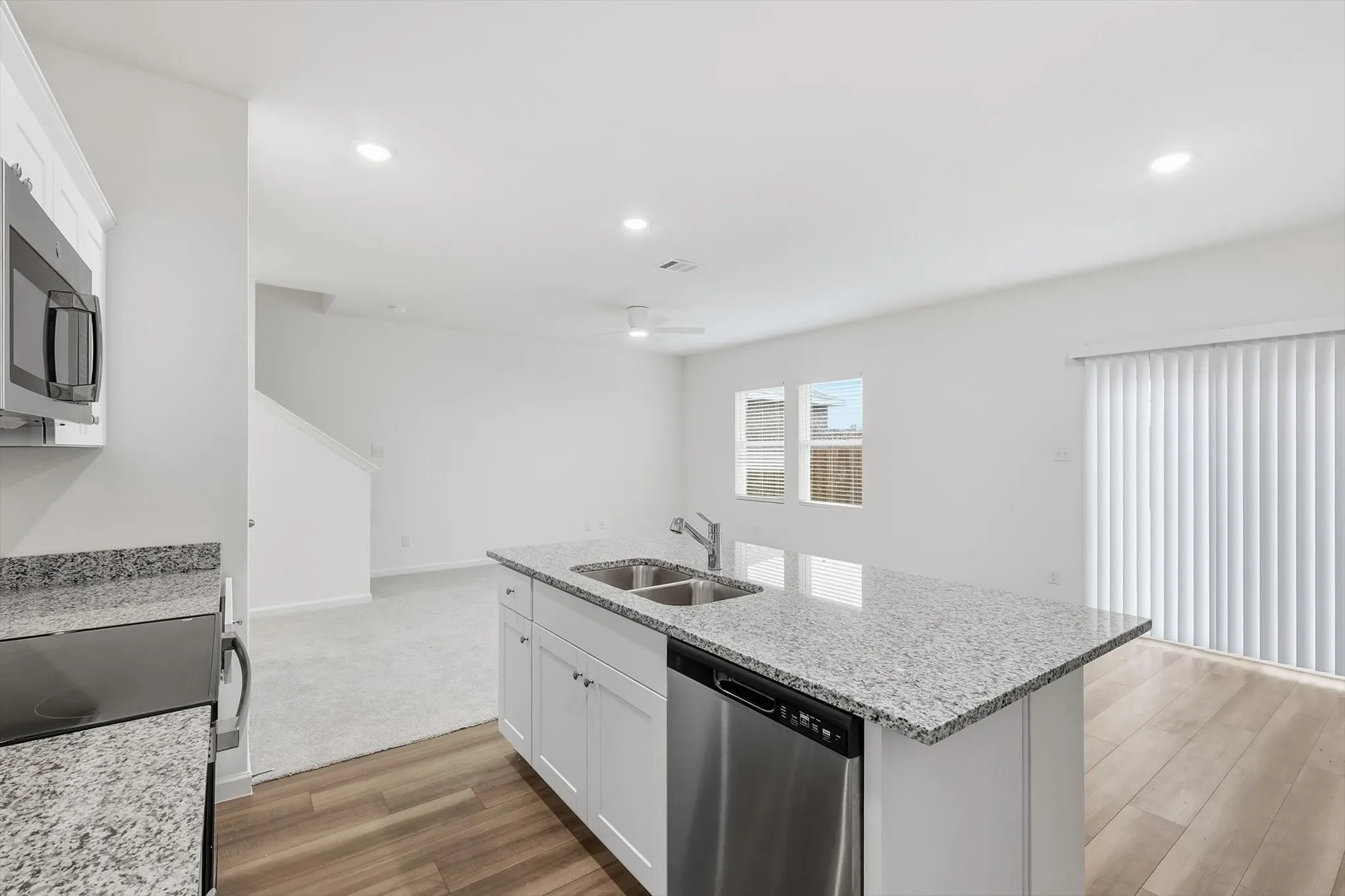 Open-concept kitchen featuring an island with a double basin sink, stainless steel dishwasher, and light-toned countertops