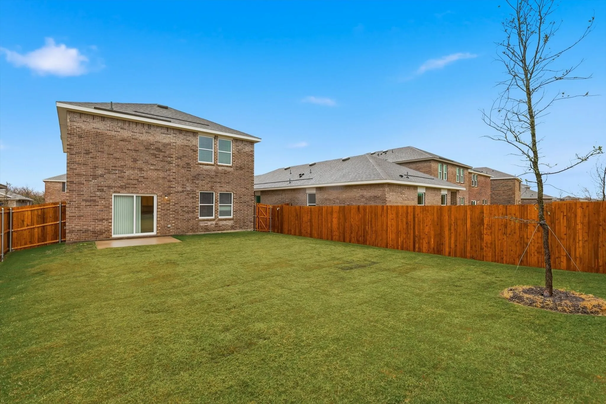 Spacious backyard featuring a manicured lawn, full privacy fencing, and a concrete patio