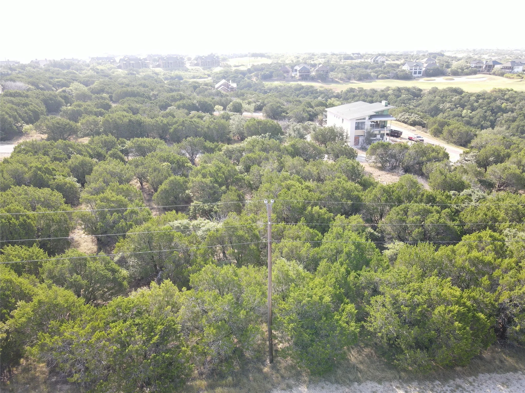 Expansive parcel featuring dense mature trees and a distant multi-story residence with multiple balconies