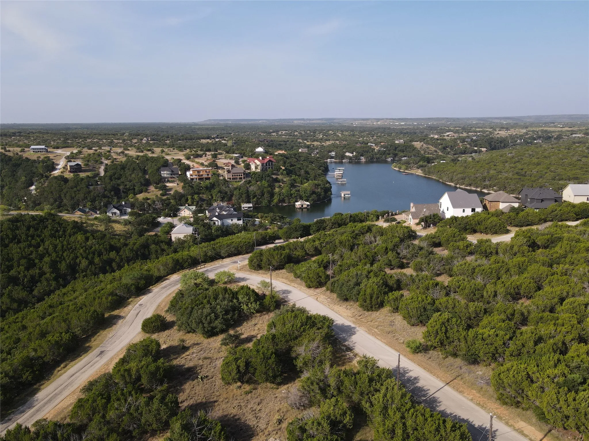 Expansive undeveloped land featuring a paved road, mature trees, and distant water frontage