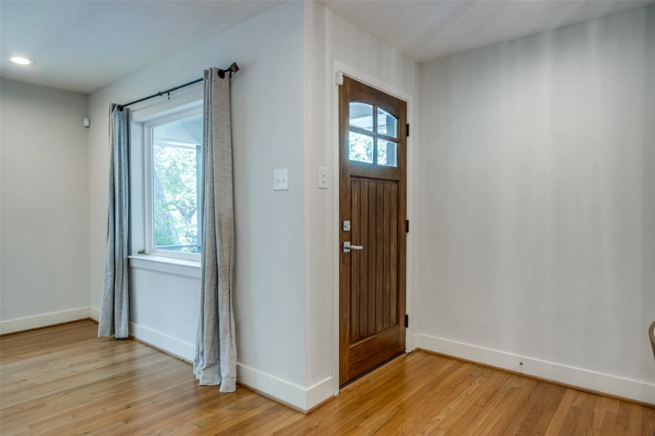 Wood-finish flooring with white baseboards, a wood entry door with glass panels, and a window with white trim