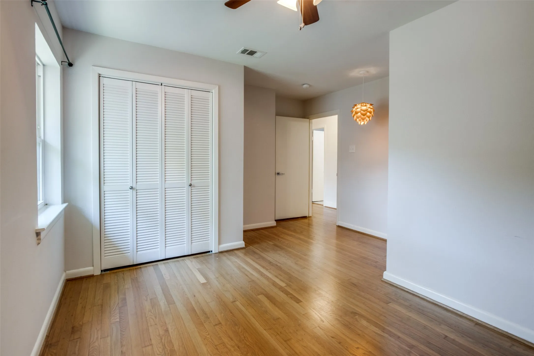 Room featuring wood-finish flooring, a double window, a louvered bi-fold closet, and a contemporary ceiling fixture