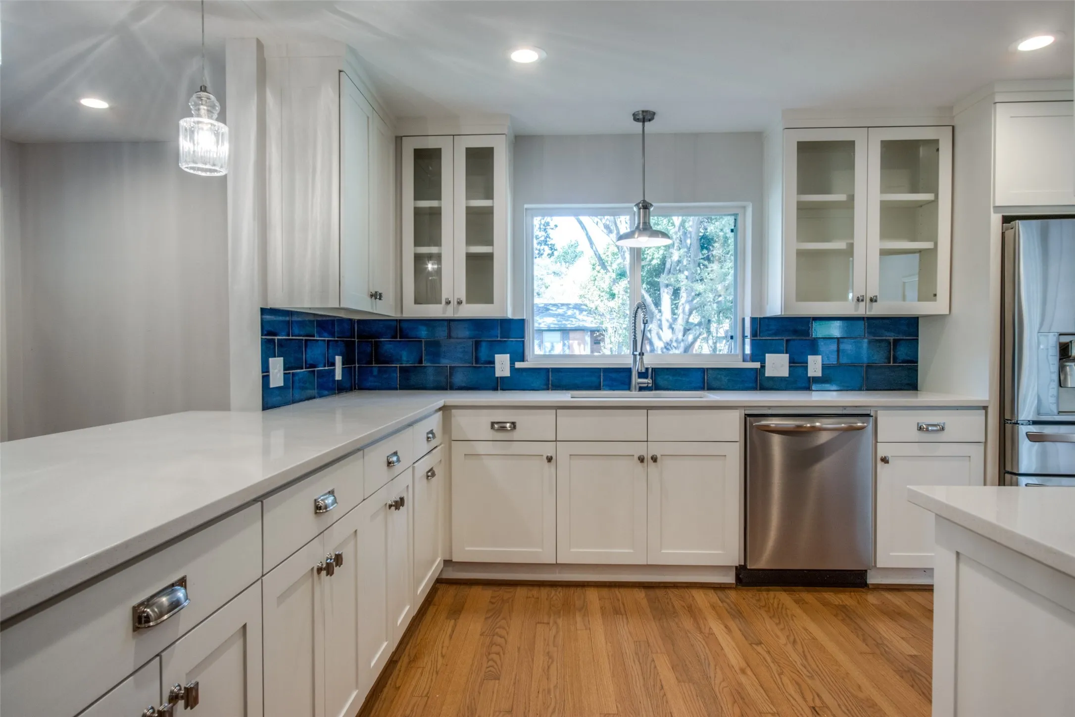 Modern kitchen featuring white cabinetry, light-colored countertops, a blue subway tile backsplash, stainless steel appliances, and wood-finish flooring
