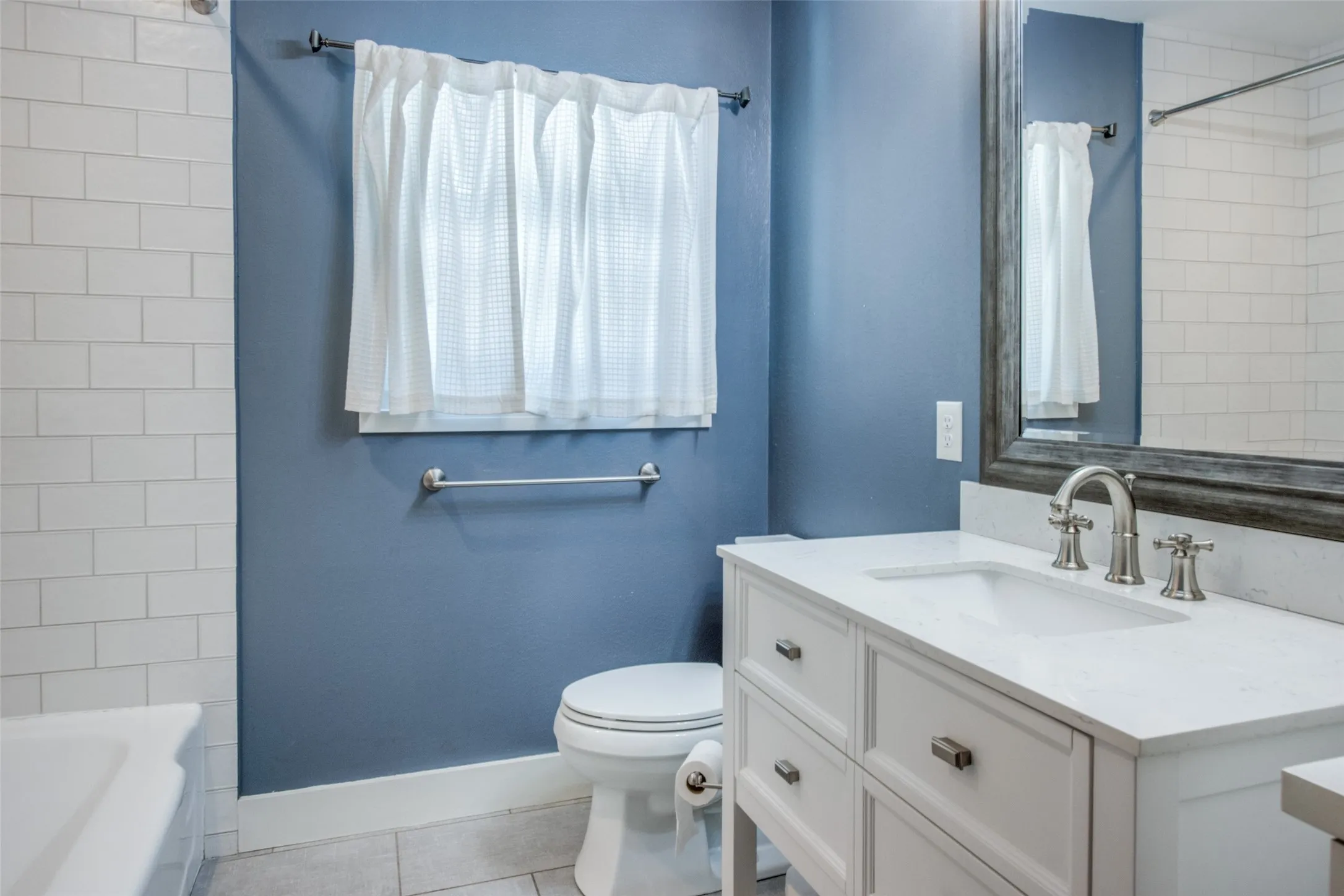 Bathroom featuring a white subway tile surround, blue painted walls, a window, a white toilet, and a vanity with an integrated sink and brushed nickel faucet