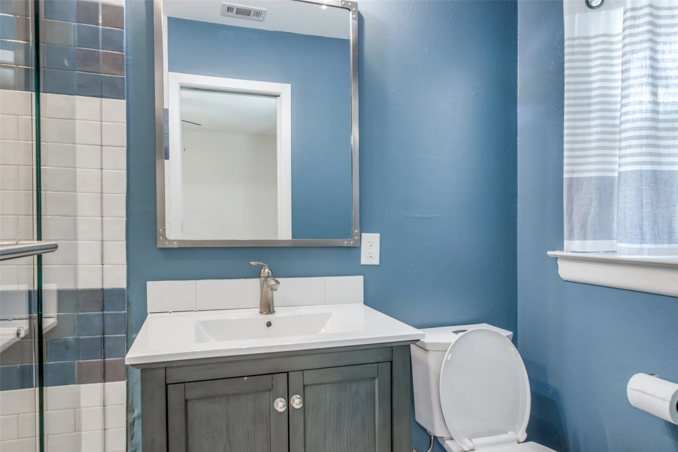 Bathroom featuring a gray vanity with an integrated sink, brushed nickel faucet, and a framed mirror