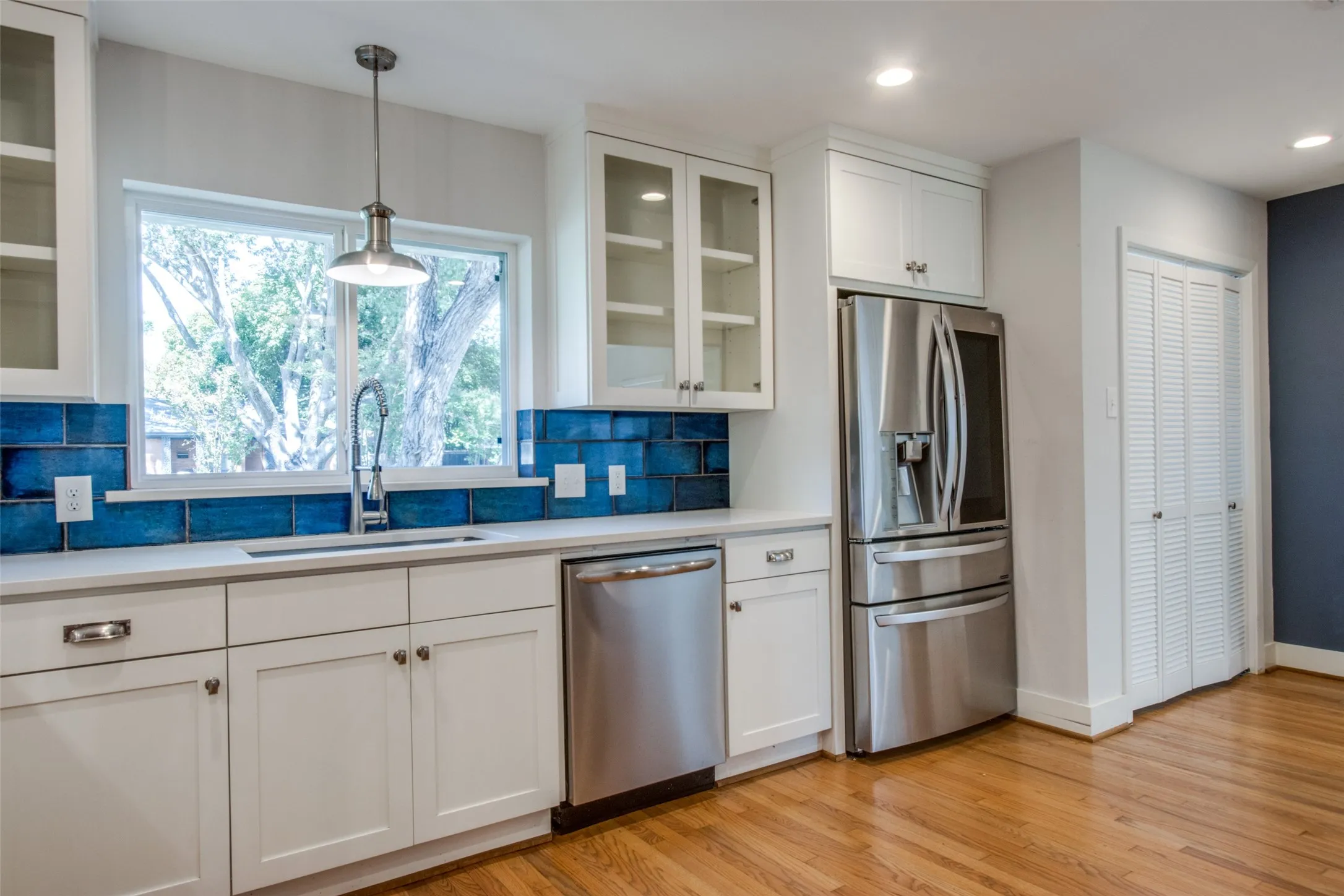 Kitchen featuring white cabinetry, stainless steel appliances, a deep blue tile backsplash, a window over the sink, and wood-finish flooring