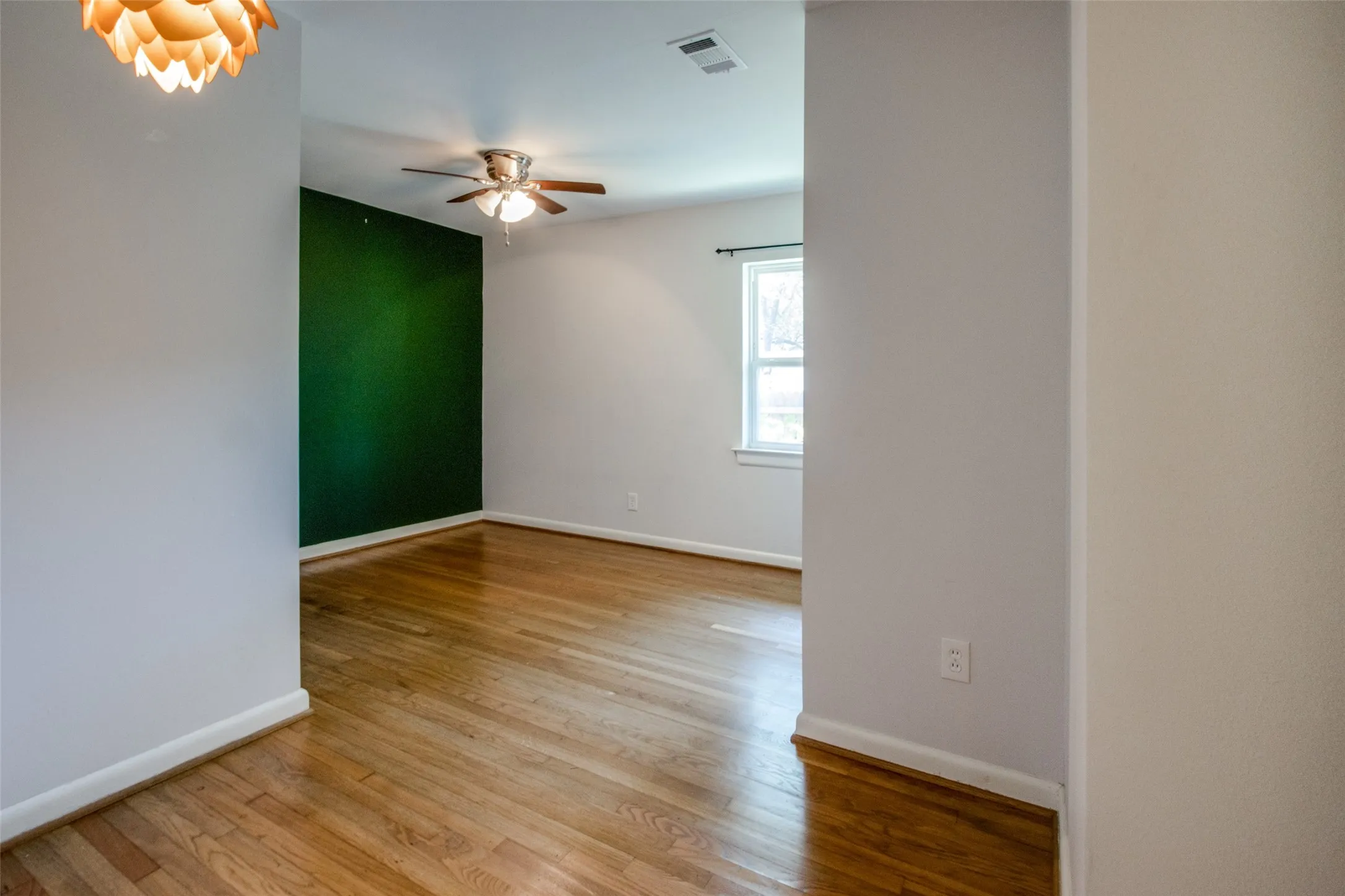 Room featuring wood-finish flooring, a distinct green accent wall, and a ceiling fan with integrated lighting