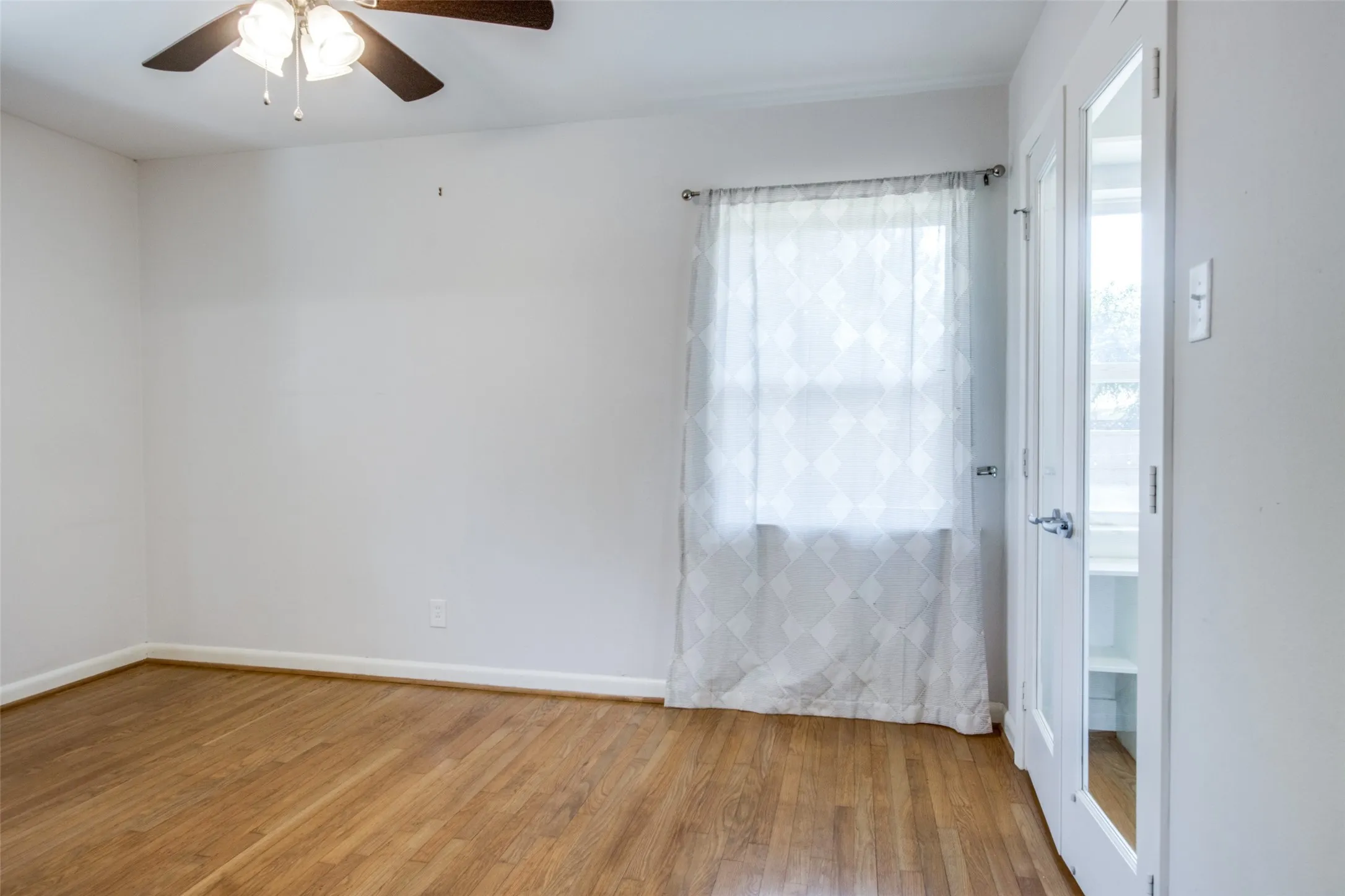Room featuring wood-finish flooring, a ceiling fan, and a window with sheer curtains