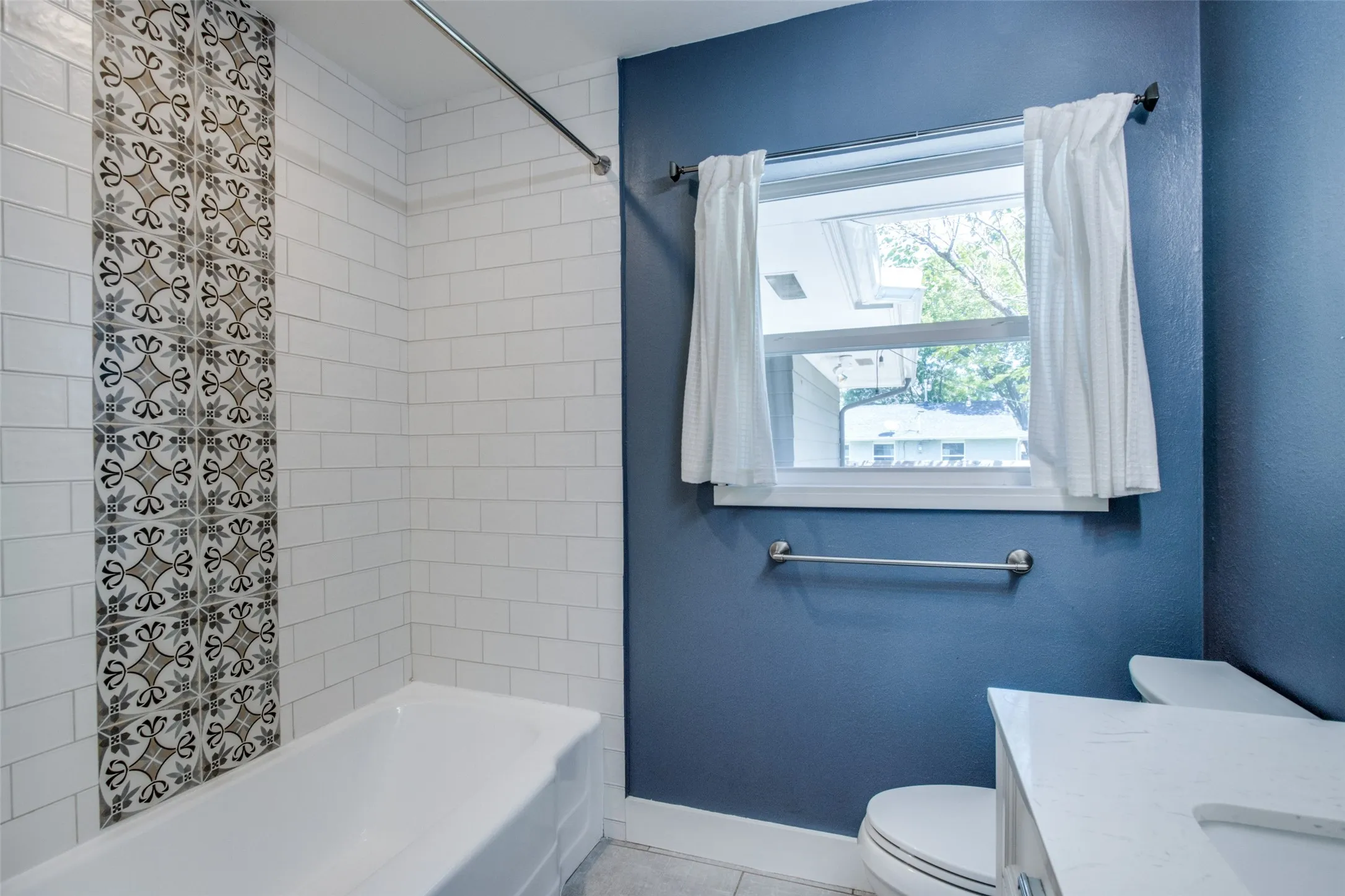 Bathroom featuring a white bathtub with subway tile surround and decorative accent tile, a window with natural light, a white vanity with integrated sink, and a toilet