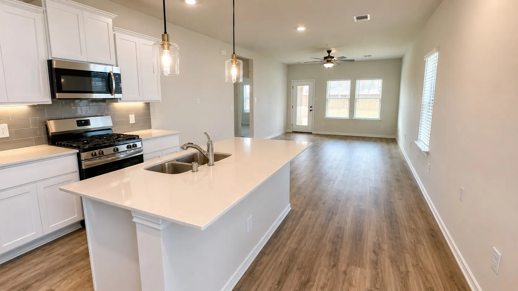 Kitchen island with dual basin sink, integrated stainless steel appliances, and white shaker cabinetry