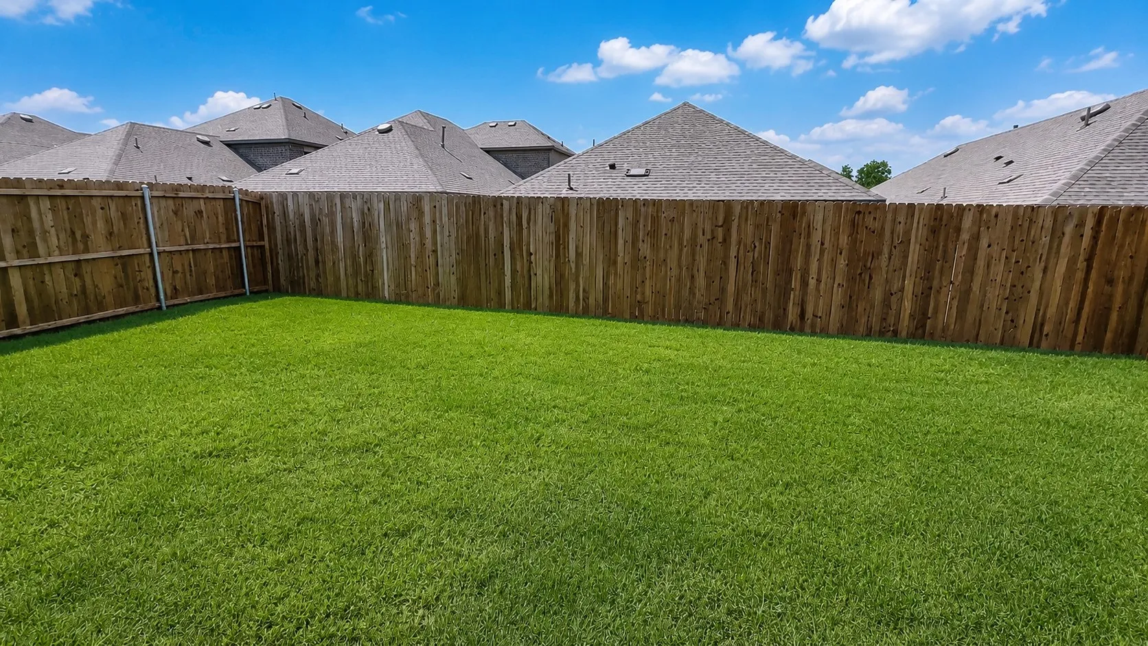 Expansive backyard featuring a lush green lawn, full wood fencing, and a clear sky overhead