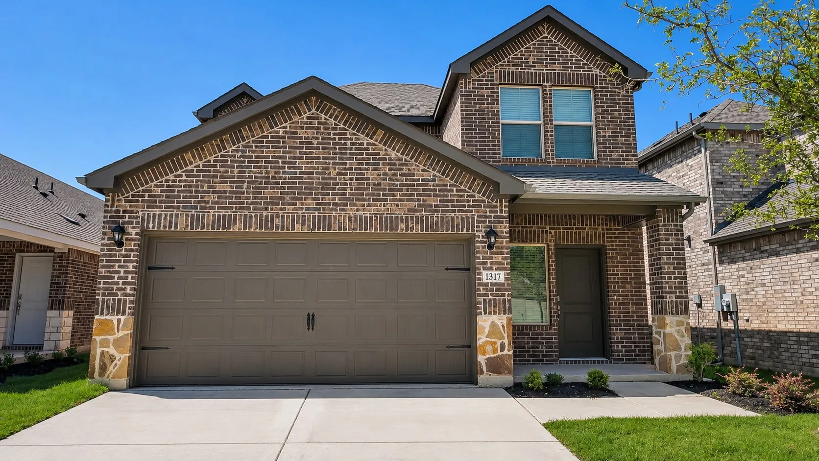Stunning two-story brick home featuring a three-car garage with dark panel doors, arched gable roofline with decorative brick detailing, and a professionally finished driveway