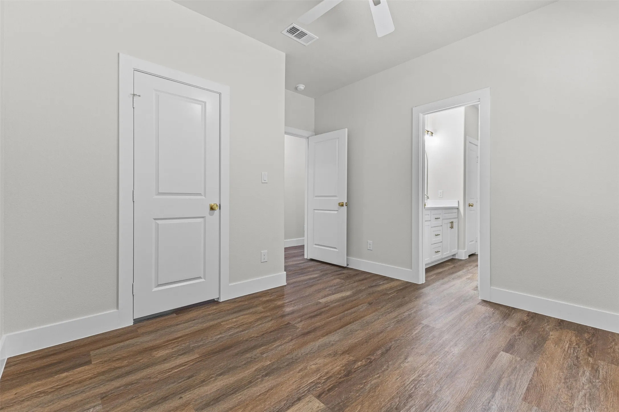 Spacious room featuring wood-finish flooring, white trim, and a ceiling fan