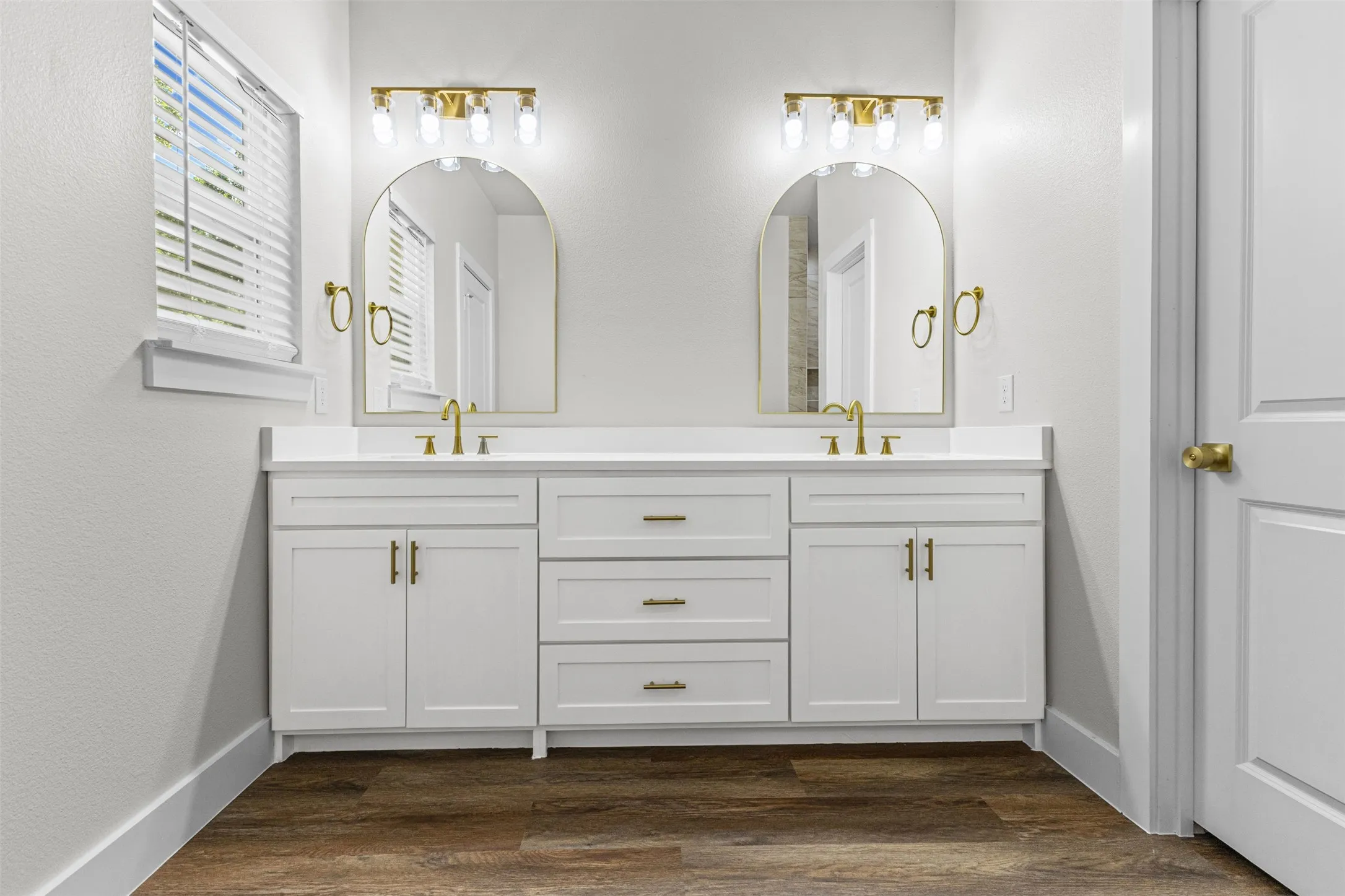 Dual vanity featuring white shaker-style cabinetry, a white countertop, and gold-finish hardware