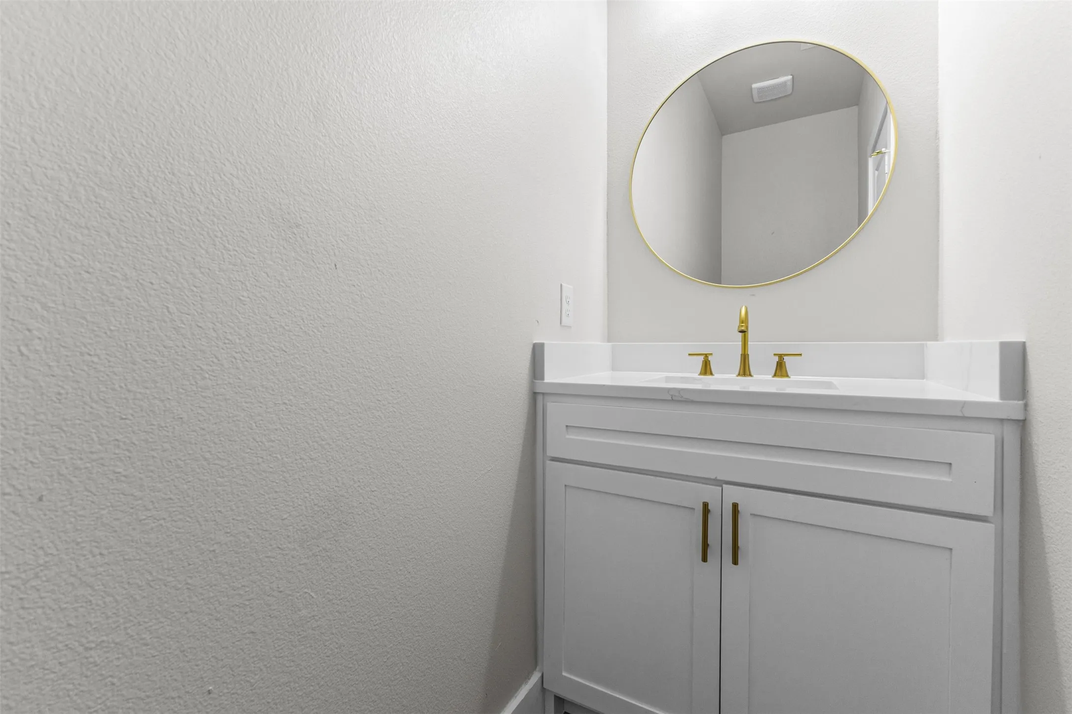 Powder room featuring a white shaker-style vanity with brass hardware, a white countertop, and a contemporary gold-framed oval mirror