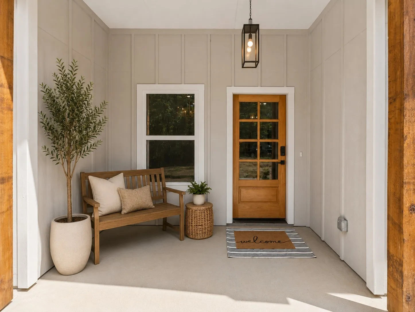 Covered front entry featuring a wood-panel door with windowpanes, board and batten siding, a single window, an overhead light fixture, and concrete flooring