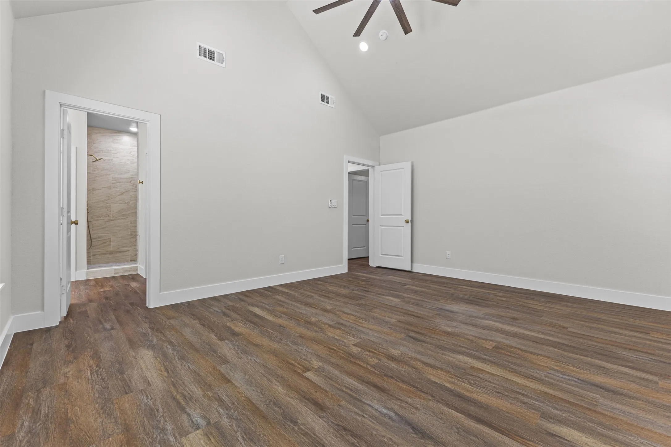 Spacious room featuring vaulted ceilings, wood-finish flooring, and crisp white baseboards