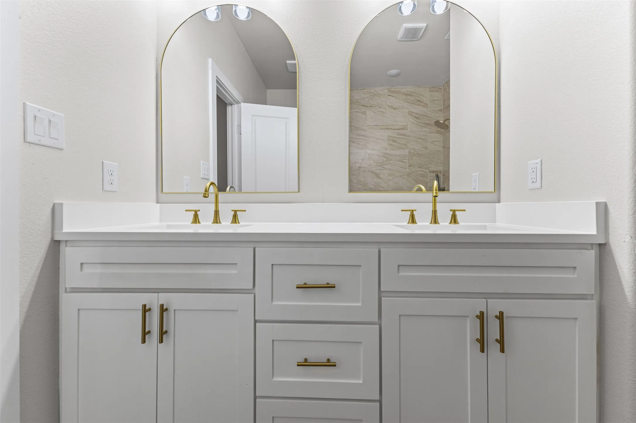 Dual white vanities with gold-toned hardware, quartz countertops, and integrated rectangular sinks