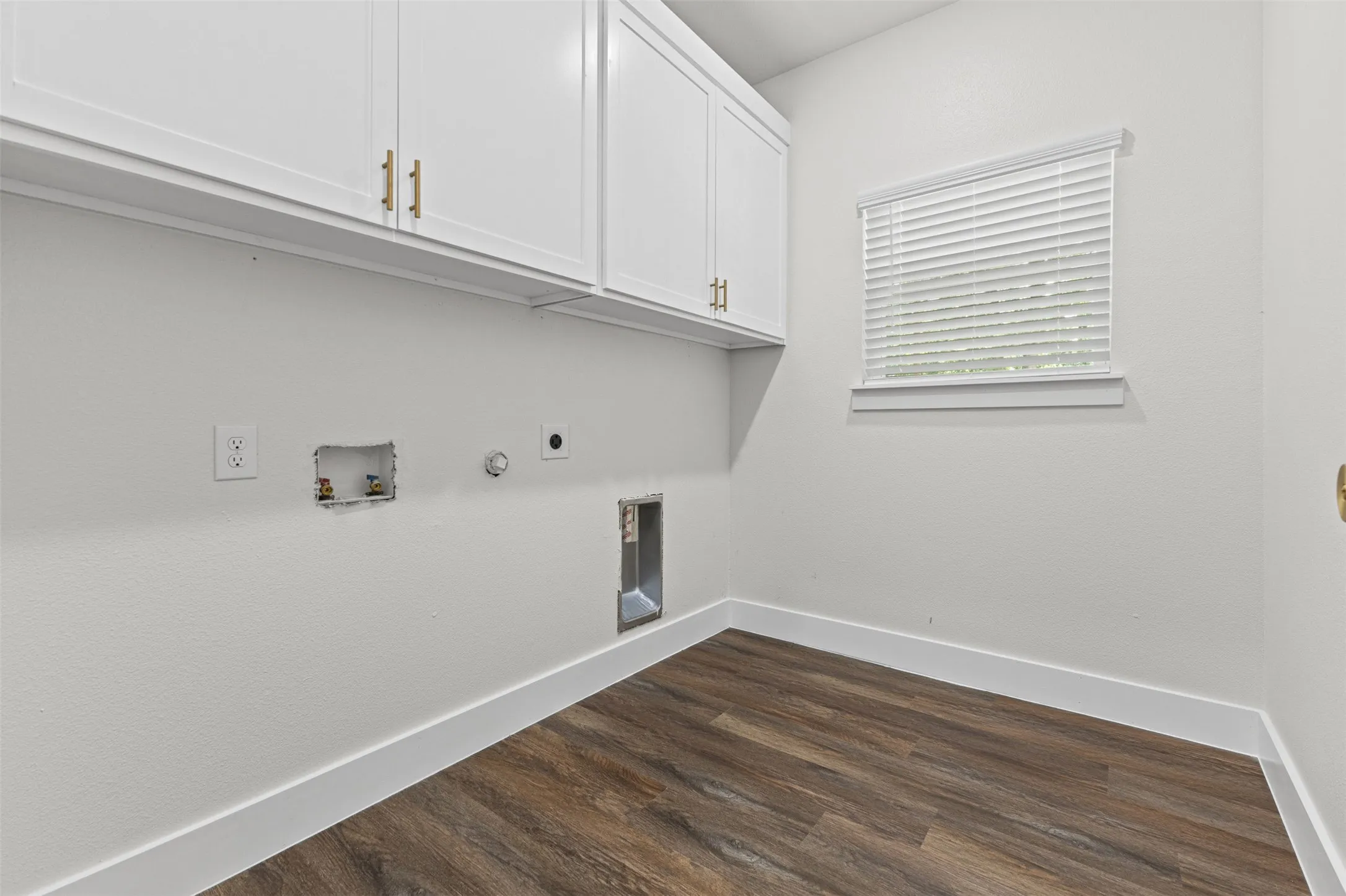 Utility room featuring white shaker cabinetry with gold-tone hardware, wood-finish flooring, white baseboards, and a window with blinds