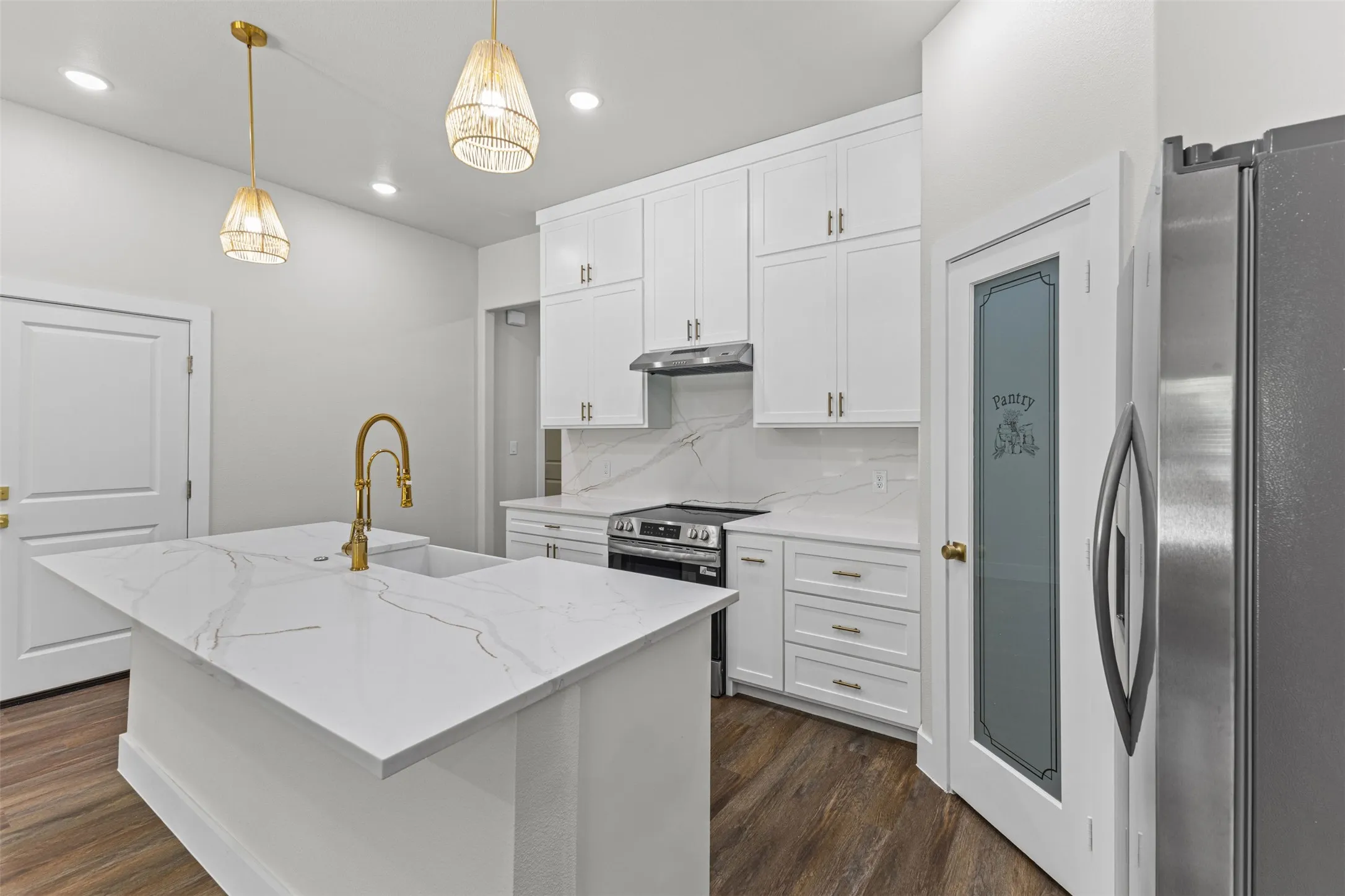 Kitchen featuring a central island with an integrated sink, white cabinetry, a gold-finish faucet, recessed lighting, and wood-finish flooring