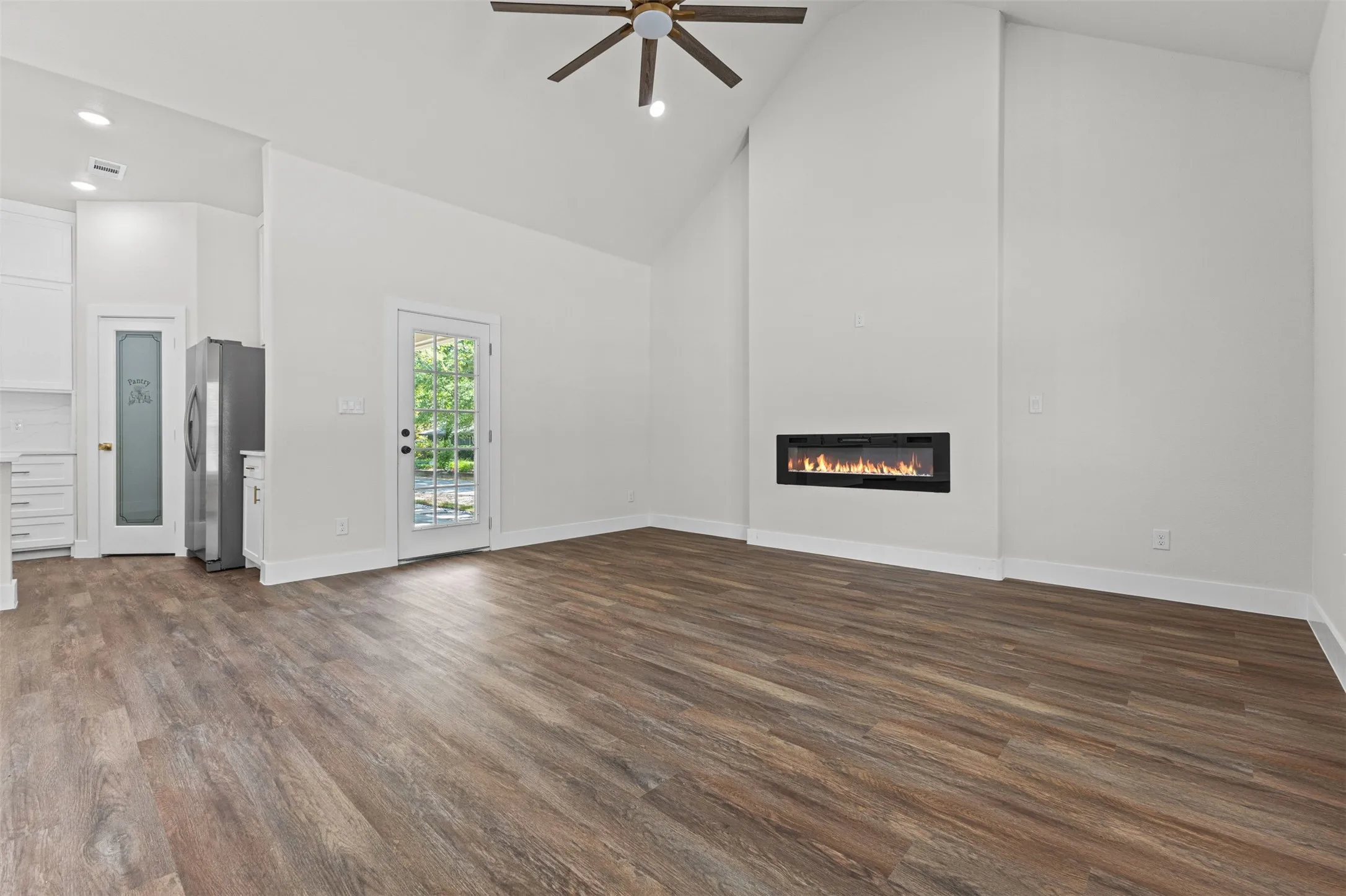Spacious interior featuring high vaulted ceilings, wood-finish flooring, a contemporary linear fireplace, and a glass-paneled door