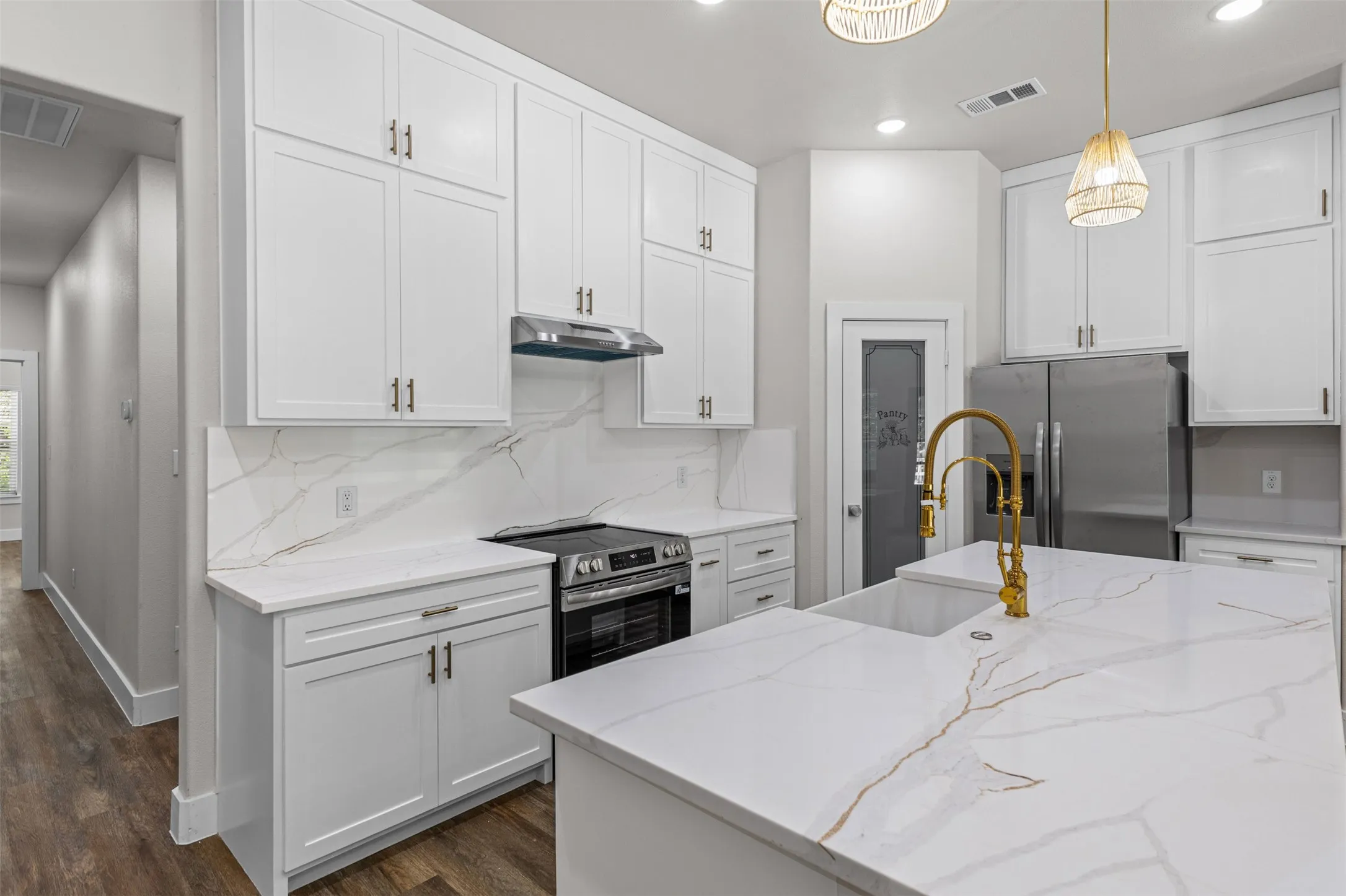 Modern kitchen featuring white shaker cabinetry with brushed gold hardware, a white stone island with a single-basin sink and gold faucet, a stainless steel range and hood, and matching white stone countertops and backsplash