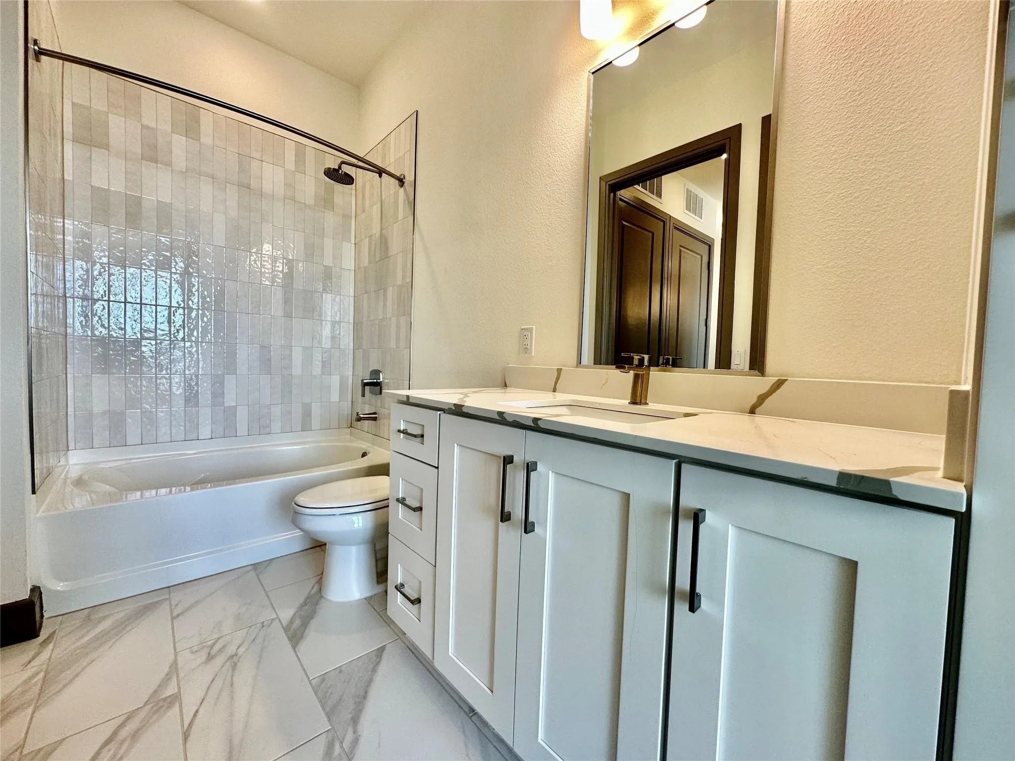 Bathroom featuring a white vanity with slab cabinet doors and matte black hardware, a light-toned countertop with veining, and a large mirror