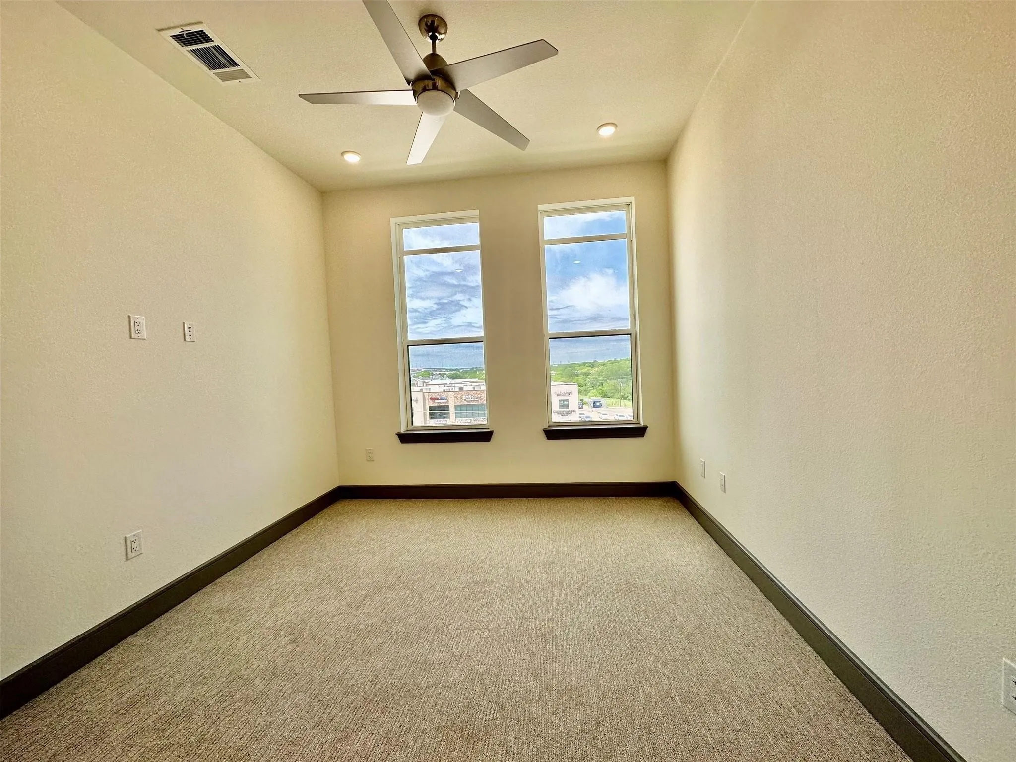 Carpeted room with two large windows, dark baseboards, and a ceiling fan with integrated lighting