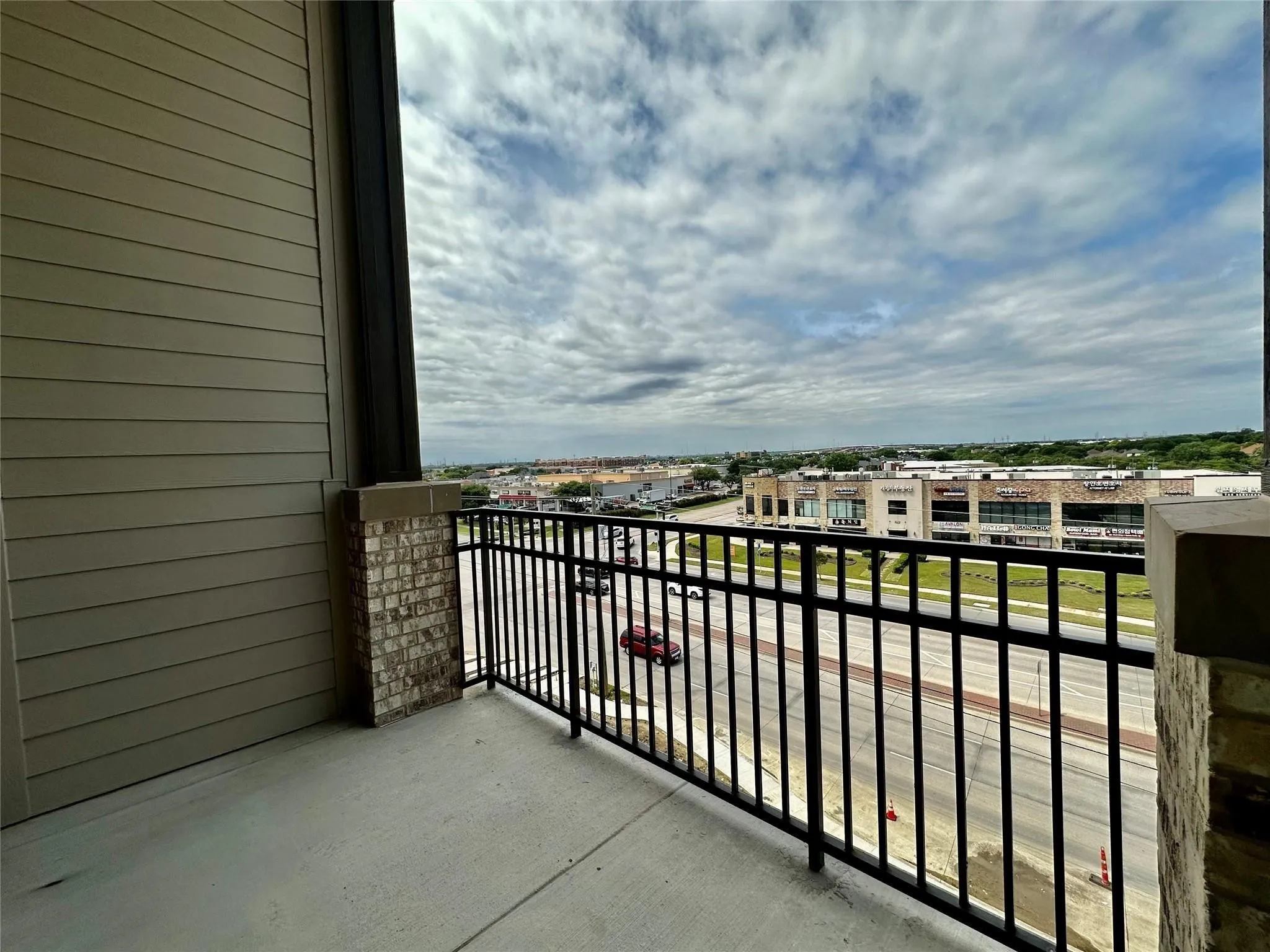 Balcony featuring a concrete surface, black metal railing, and brick column accents