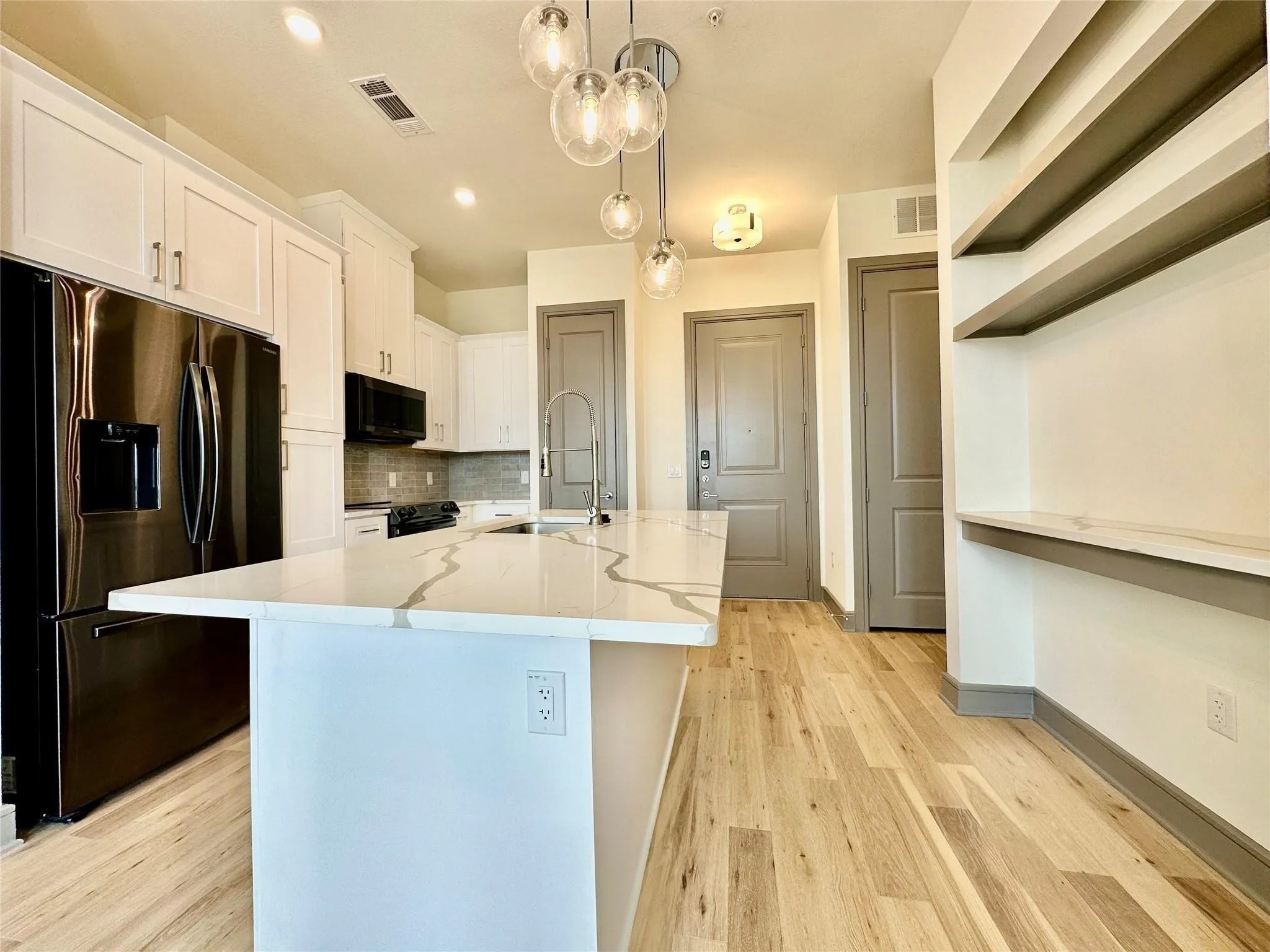 Kitchen featuring a large island with a waterfall-edge countertop, stainless steel appliances, white cabinetry, and wood-finish flooring