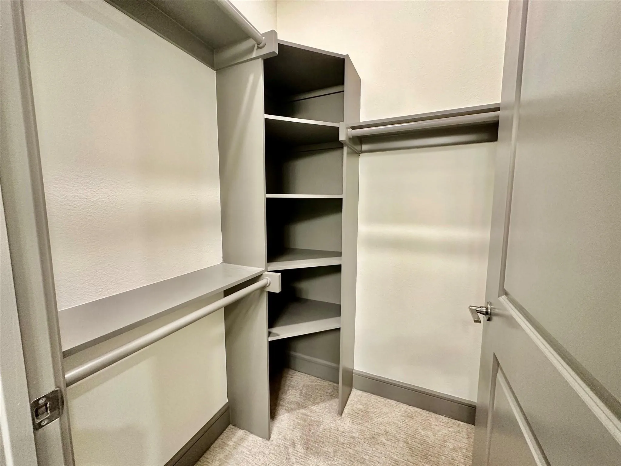 Built-in closet system featuring multiple hanging rods, corner shelving, and neutral carpeting