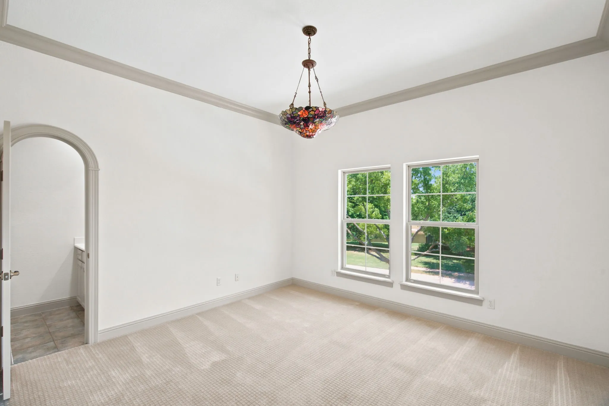 Coved ceiling with crown molding, two large windows, arched doorway, and built-in vanity with tiled flooring