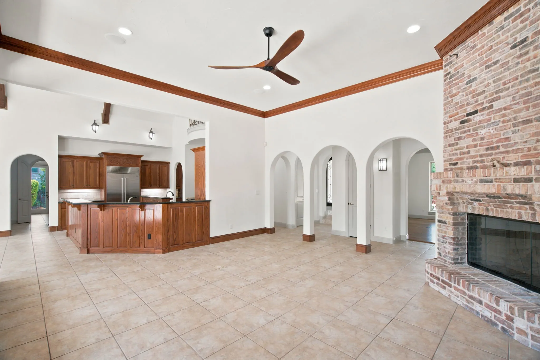 Living area featuring a brick fireplace, tiled flooring, wood-finish ceiling fan, and arched architectural details
