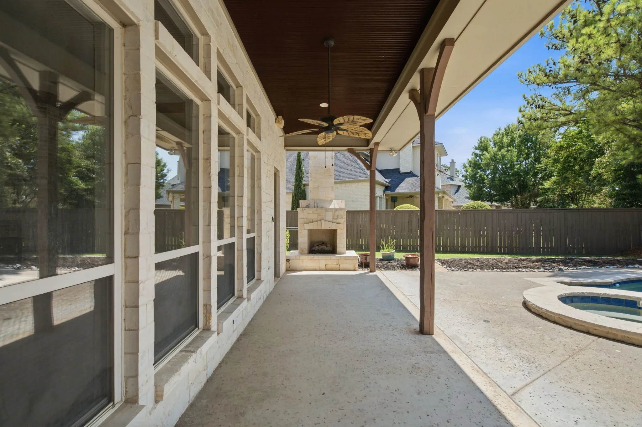 Covered patio featuring a stone fireplace, ceiling fan, and concrete flooring