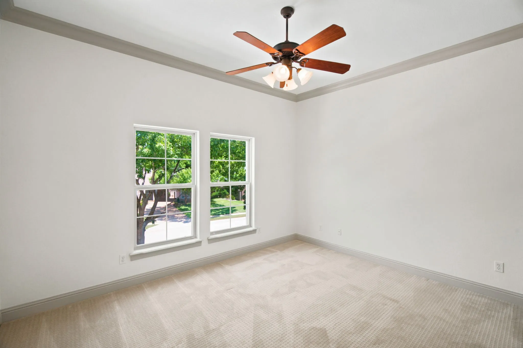 Neutral tone walls, recessed ceiling with crown molding, ceiling fan with integrated lighting, two double-hung windows, and carpeted flooring