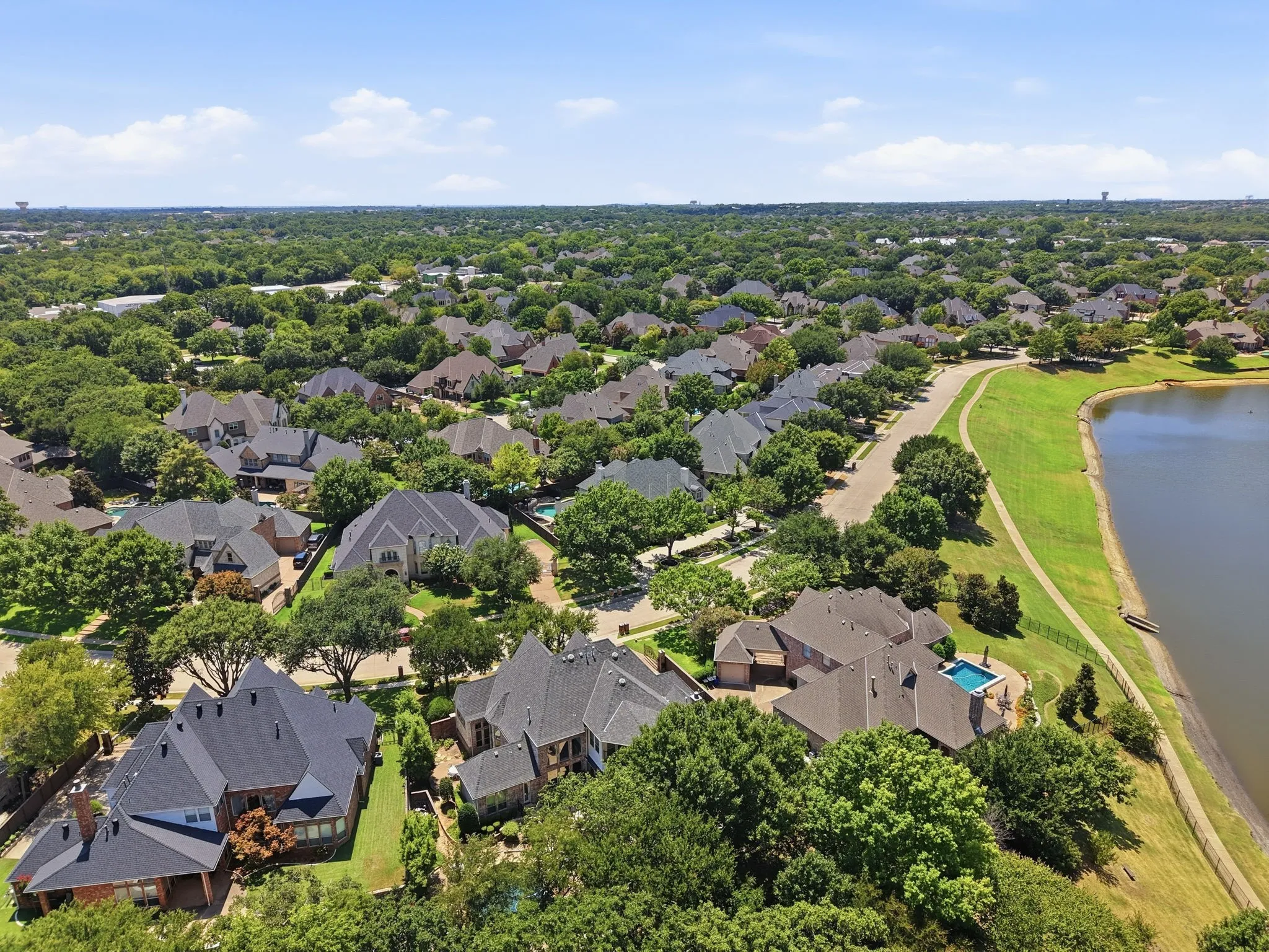 Lakeside property with a private pool, surrounded by mature trees and residential landscaping