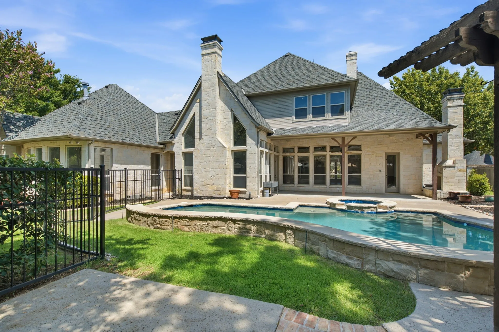 Expansive backyard featuring a swimming pool with integrated spa, stone retaining wall, and a covered patio