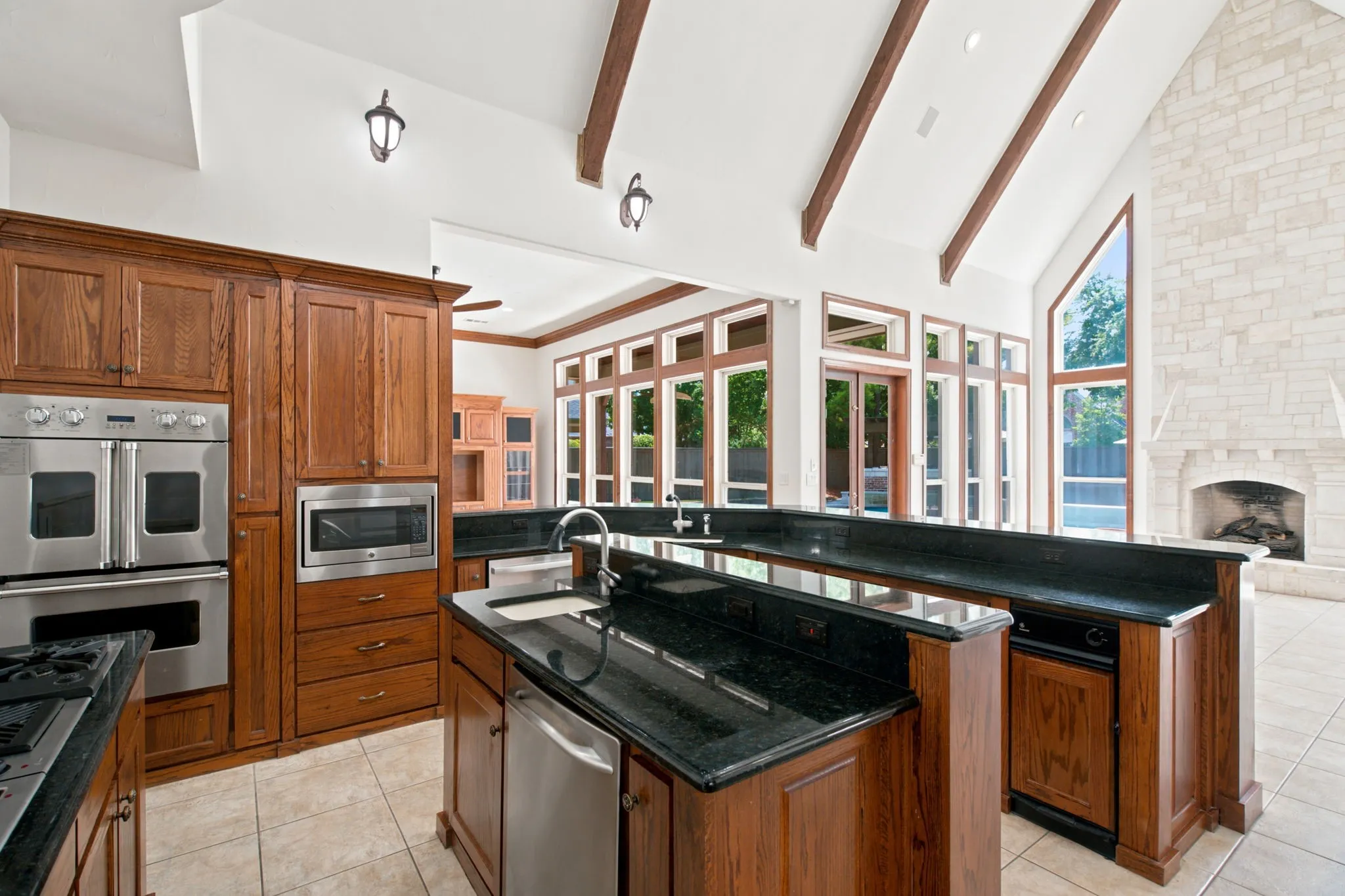 Kitchen featuring wood cabinetry, stainless steel appliances, dark stone countertops, and a center island with a sink