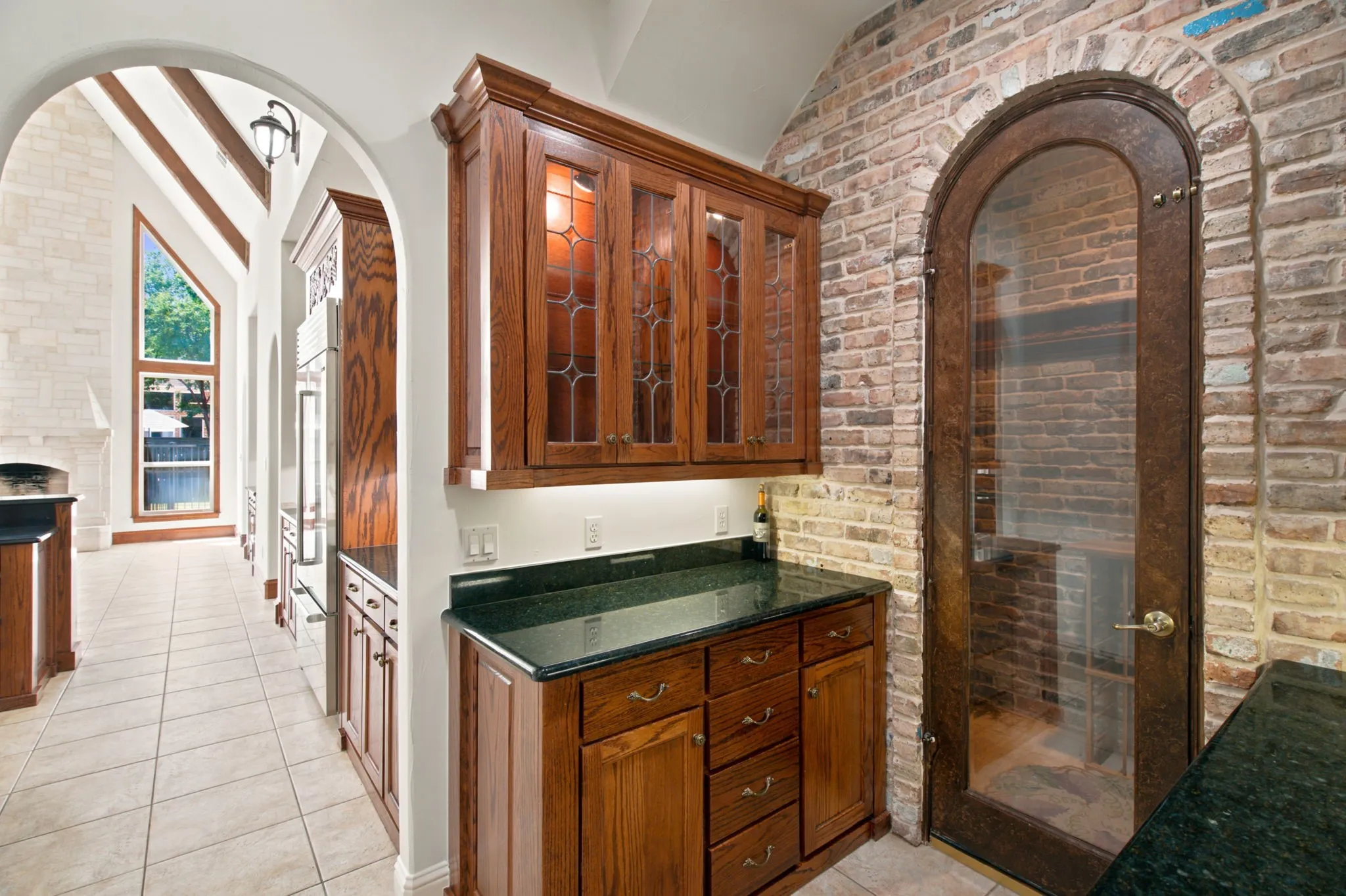 Custom wood cabinetry, dark countertops, arched doorway, floor-to-ceiling windows, and exposed brick wall