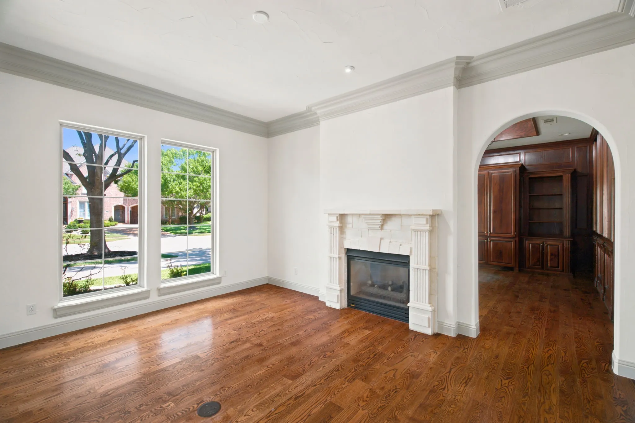Hardwood flooring, fireplace with stone surround, arched doorway, and built-in cabinetry